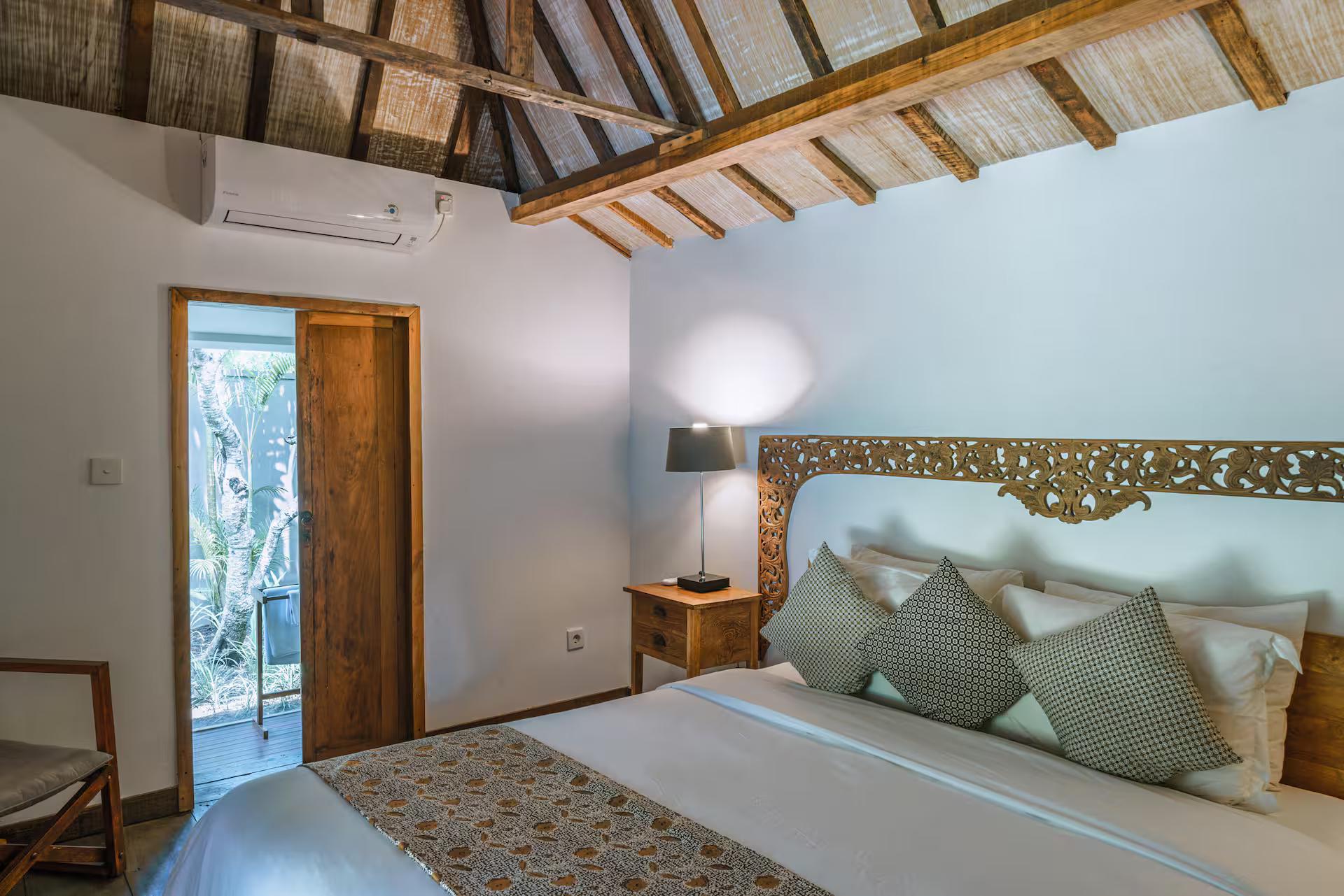 Bedroom with an antique carved timber panel above the bed and a door onto the garden