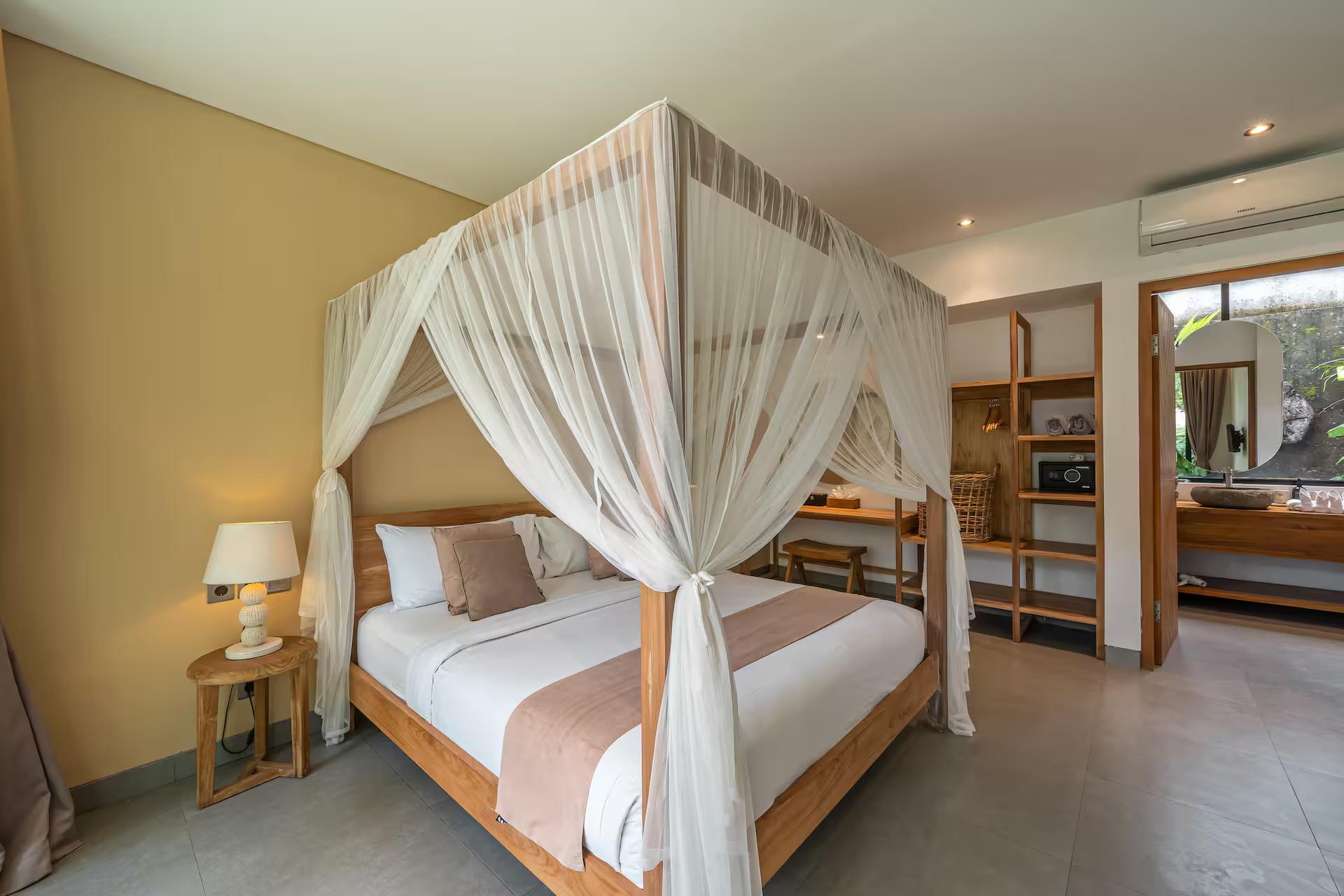 Four-poster timber bed under white voile drapes, glass doors to the garden beyond
