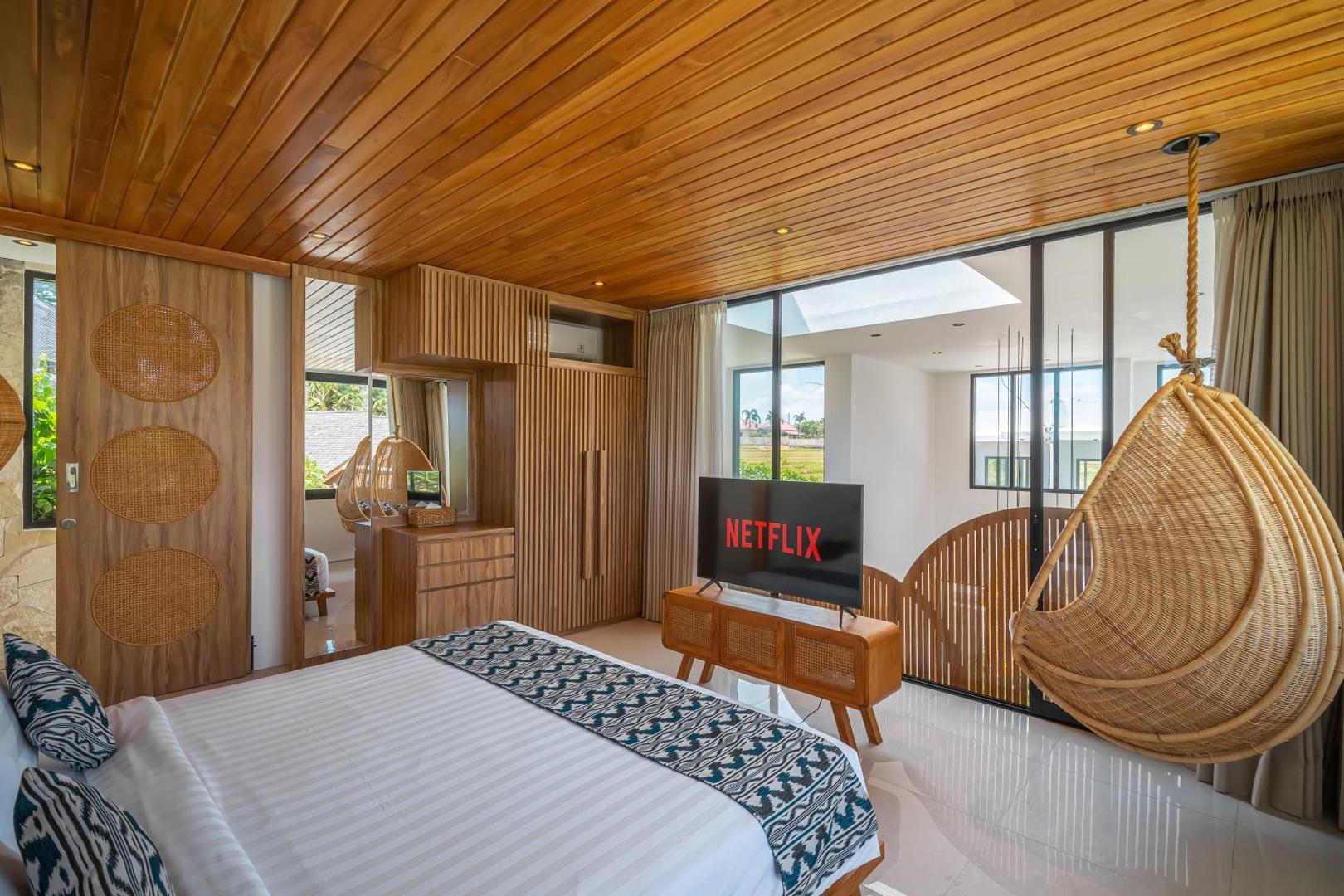 Second bedroom with a hanging rattan egg chair and a smart television on a timber console