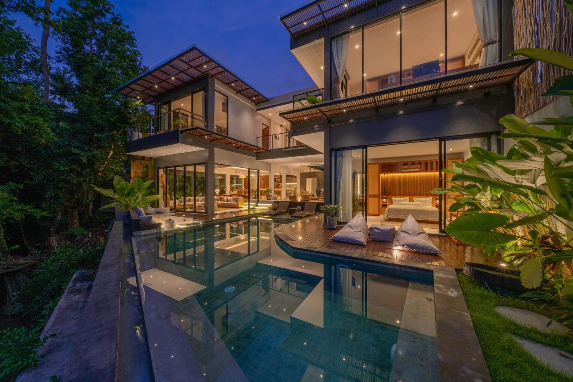 Villa Luna at dusk, interiors lit behind the glass and the pool running out towards the fields