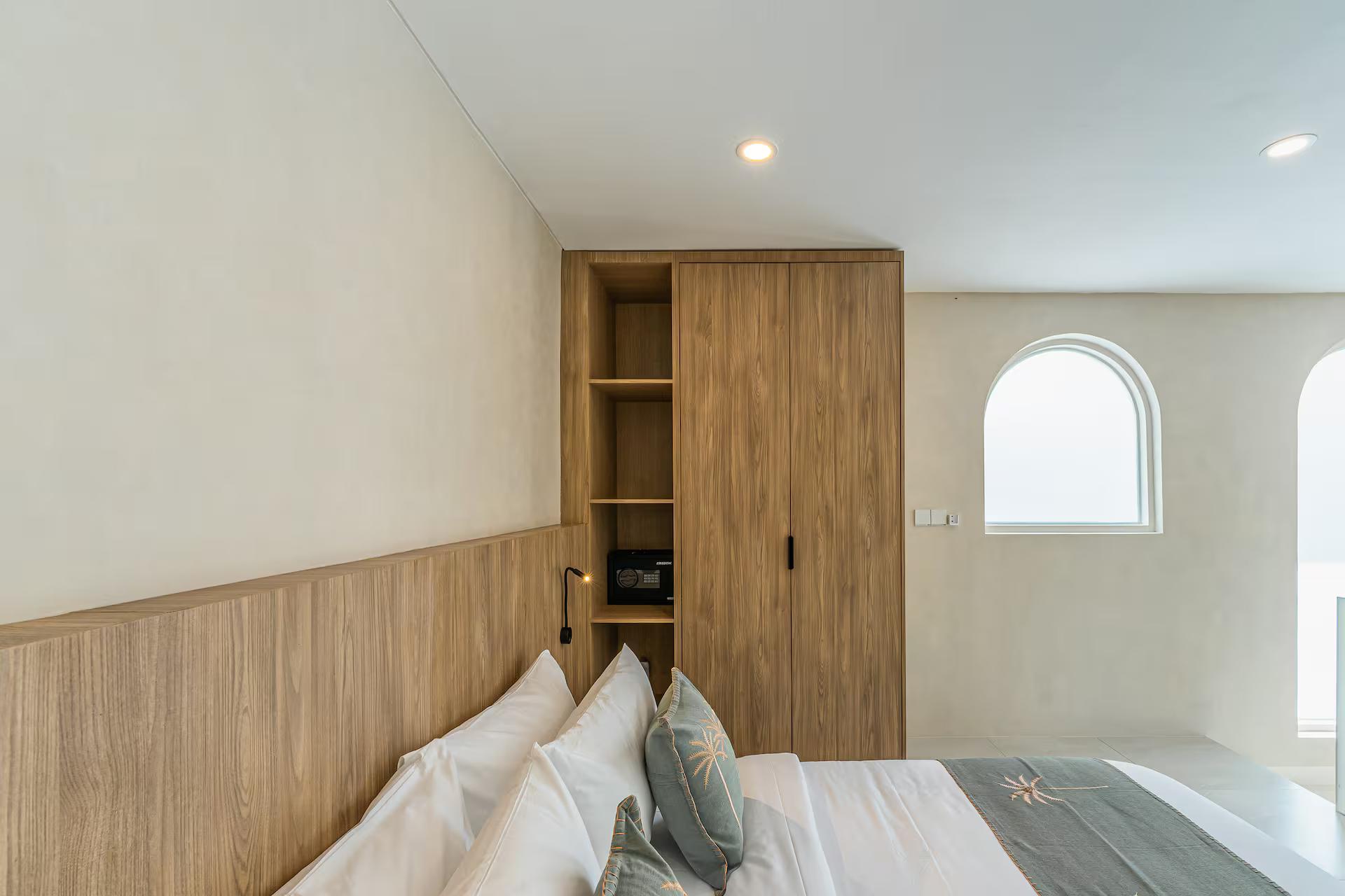 Bed against a wall of warm timber veneer with a shelf niche and an arched window