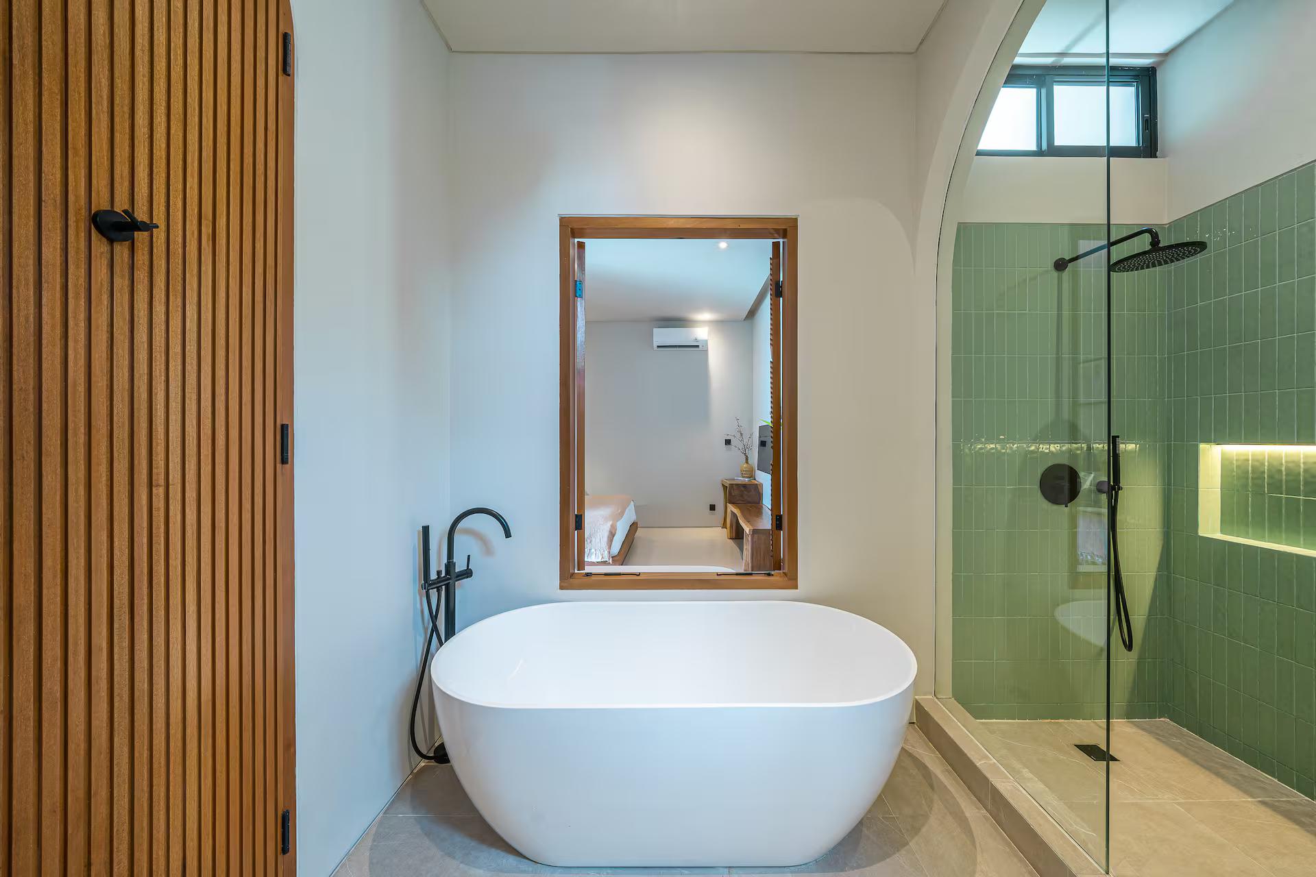 A freestanding oval bath at Casa 24 against a timber-slat wall beside a green-tiled shower
