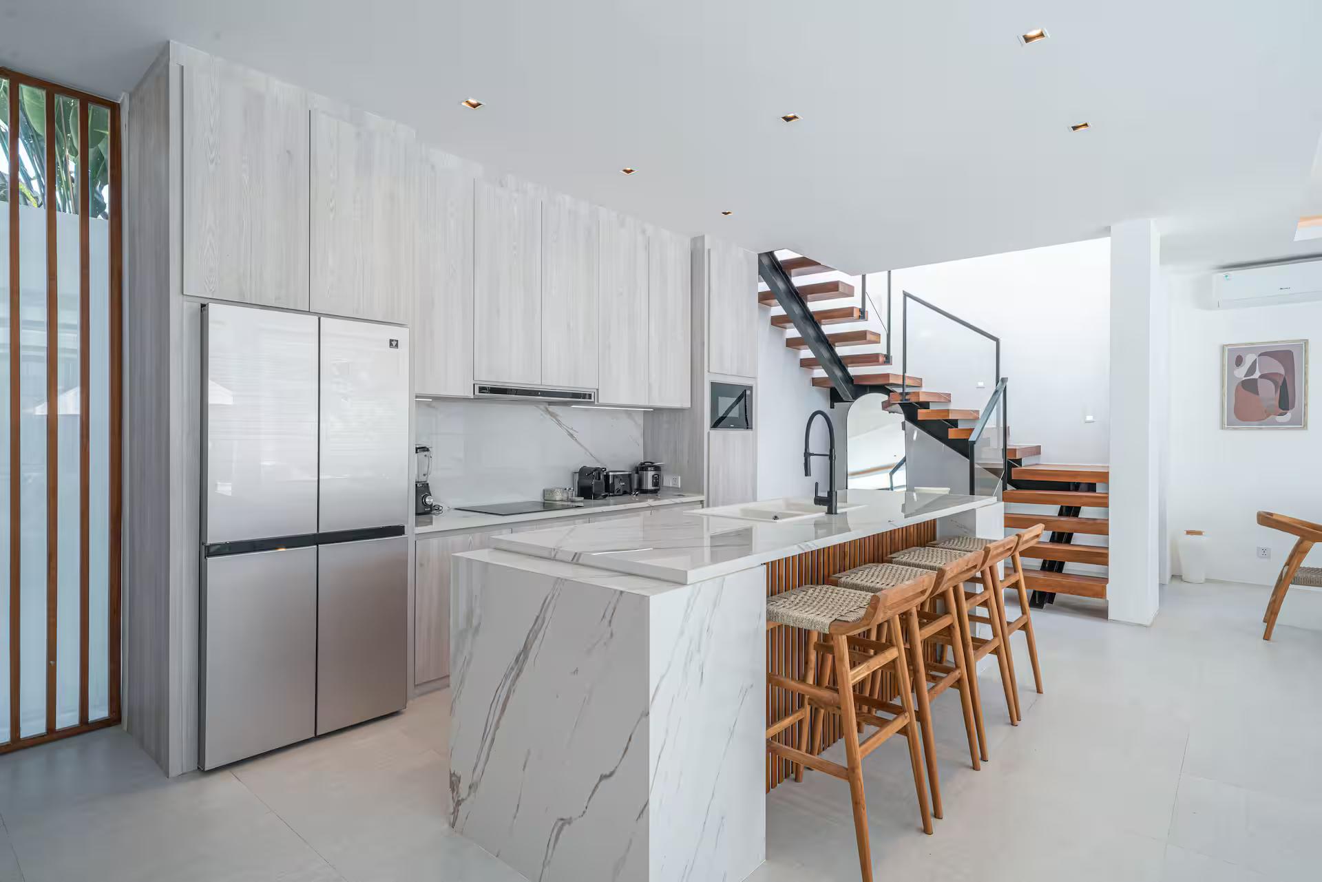 White marble kitchen island with timber bar stools at Villa Jenna, staircase alongside