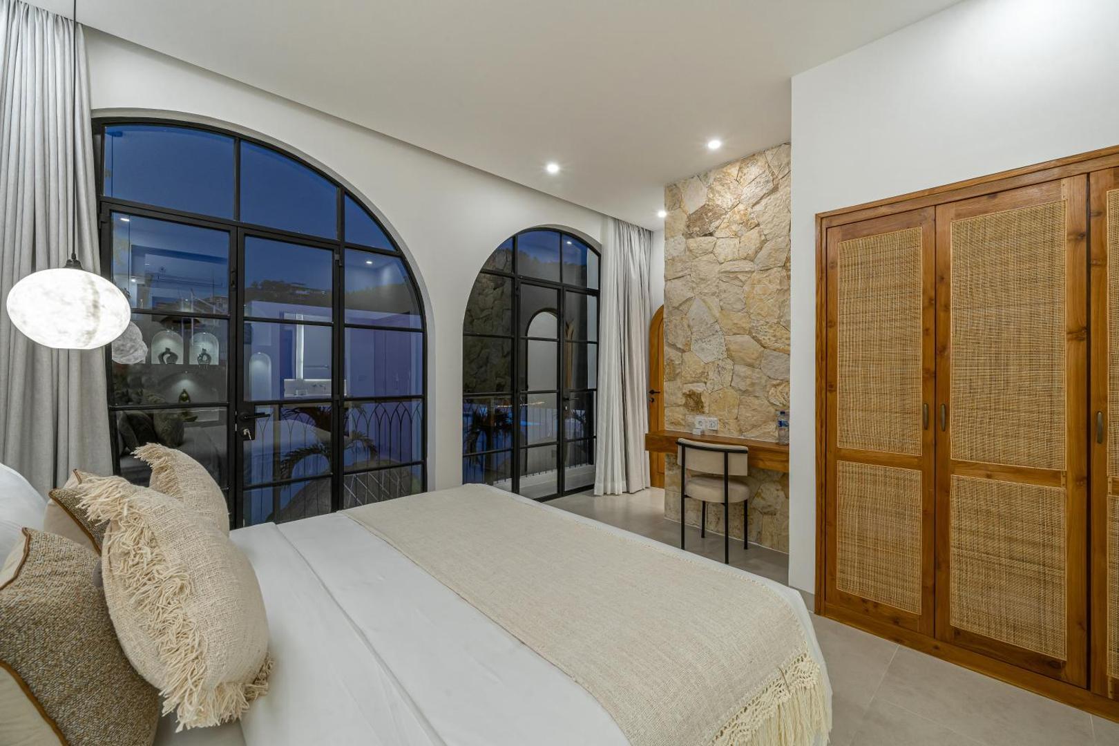 The upper bedroom at Mareo with an arched window, rattan-fronted wardrobe and stone wall