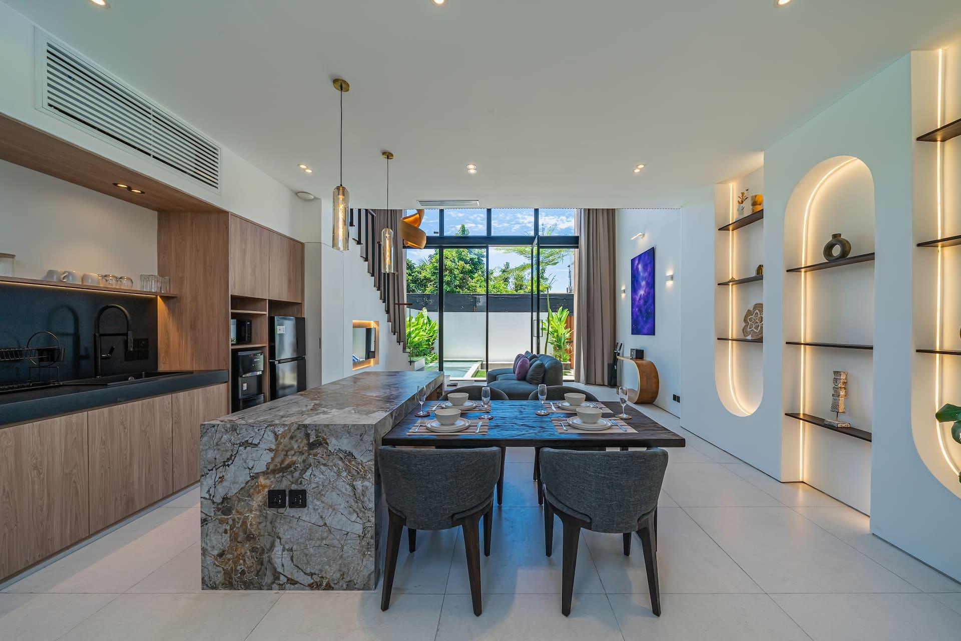 Dining table running off the stone island, lit by the arched back-lit niches of Aether Villa's white wall
