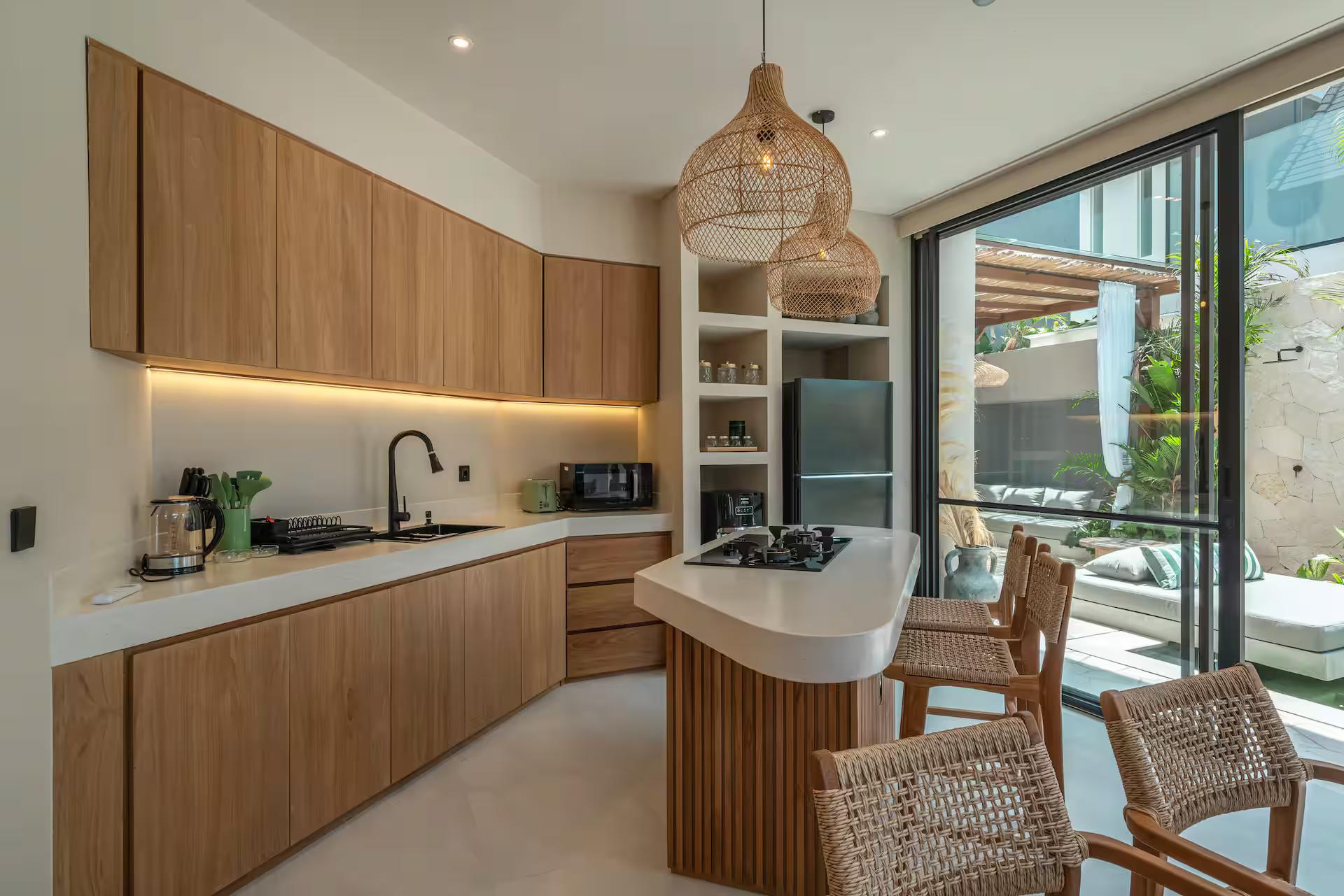 Timber kitchen at Villa Yuko with a curved stone island and woven rattan bar stools