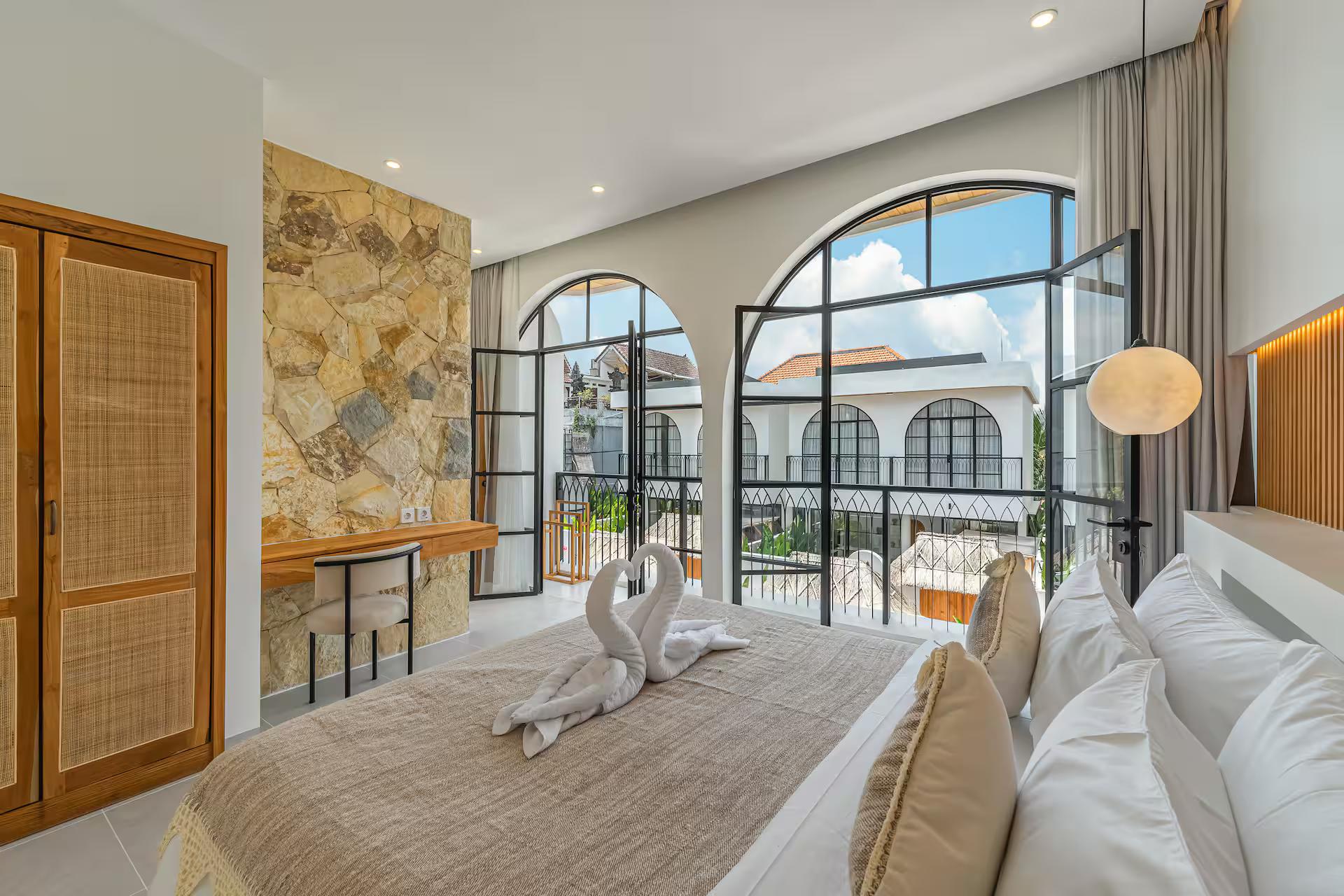 Bedroom with black-framed arched steel windows above a wall of cut limestone