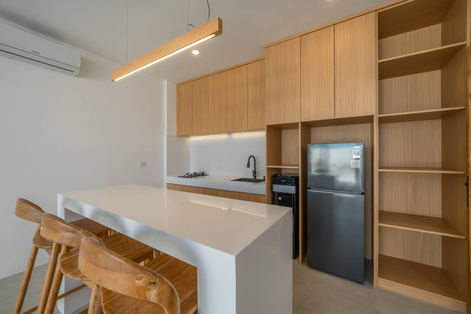 Kitchen with warm timber cabinetry, a white island and three timber bar stools