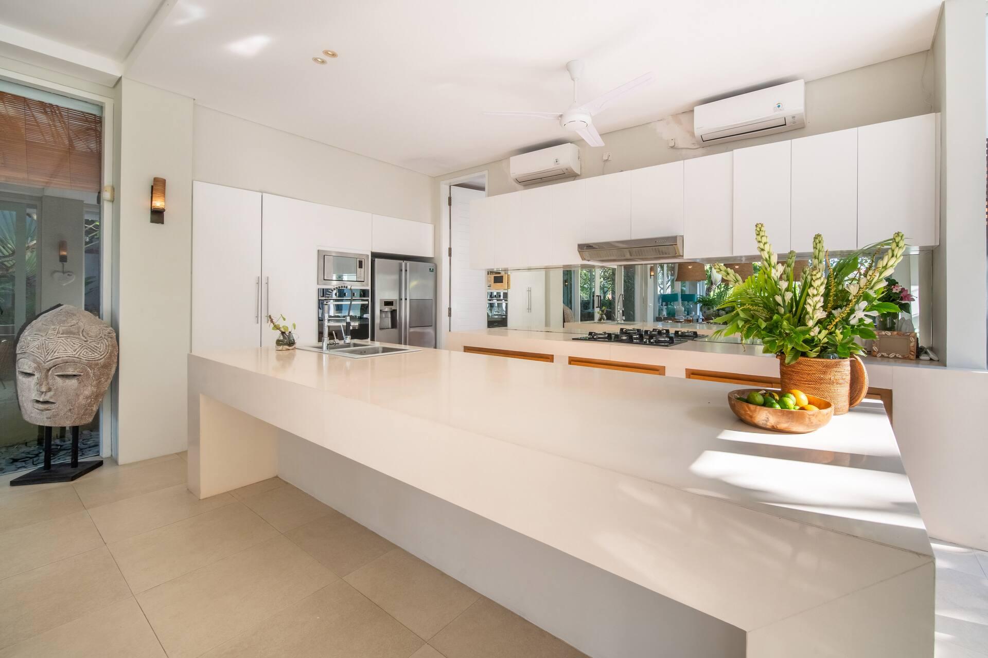Long white kitchen island, stainless appliances and a mirrored splashback overlooking the garden