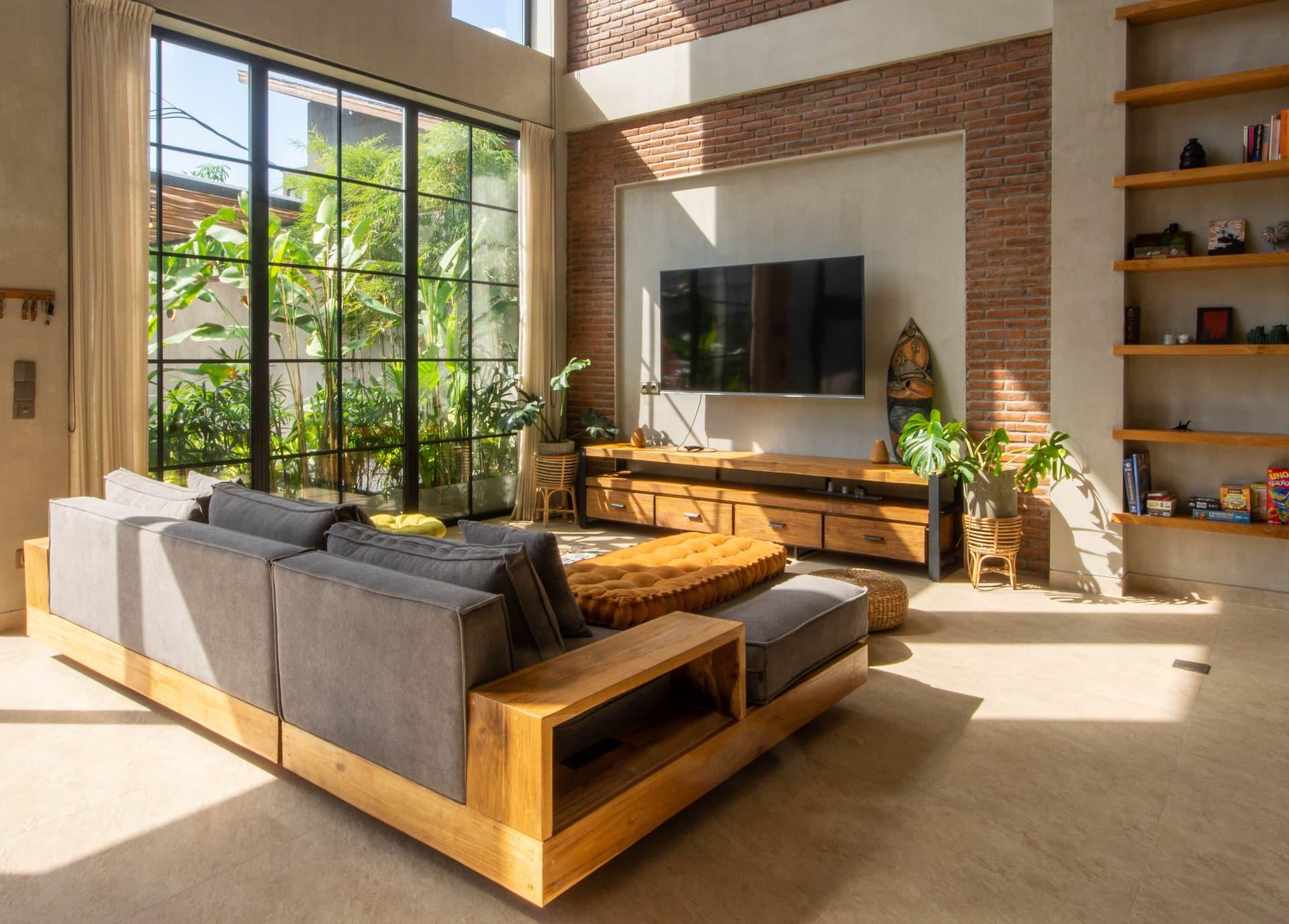 Villa Zenloft lounge with a wall-mounted TV on red brick and black-framed windows to the garden