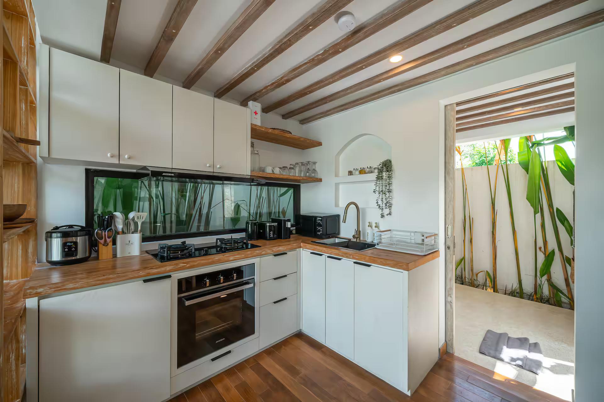 Compact kitchen with white cabinets, a timber worktop, oven and rice cooker