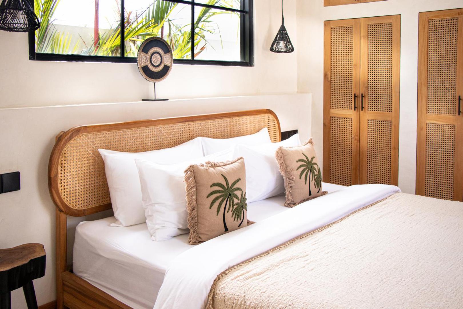 Cane headboard and palm-print cushions in a bedroom at the macan Bingin, cane wardrobes beside