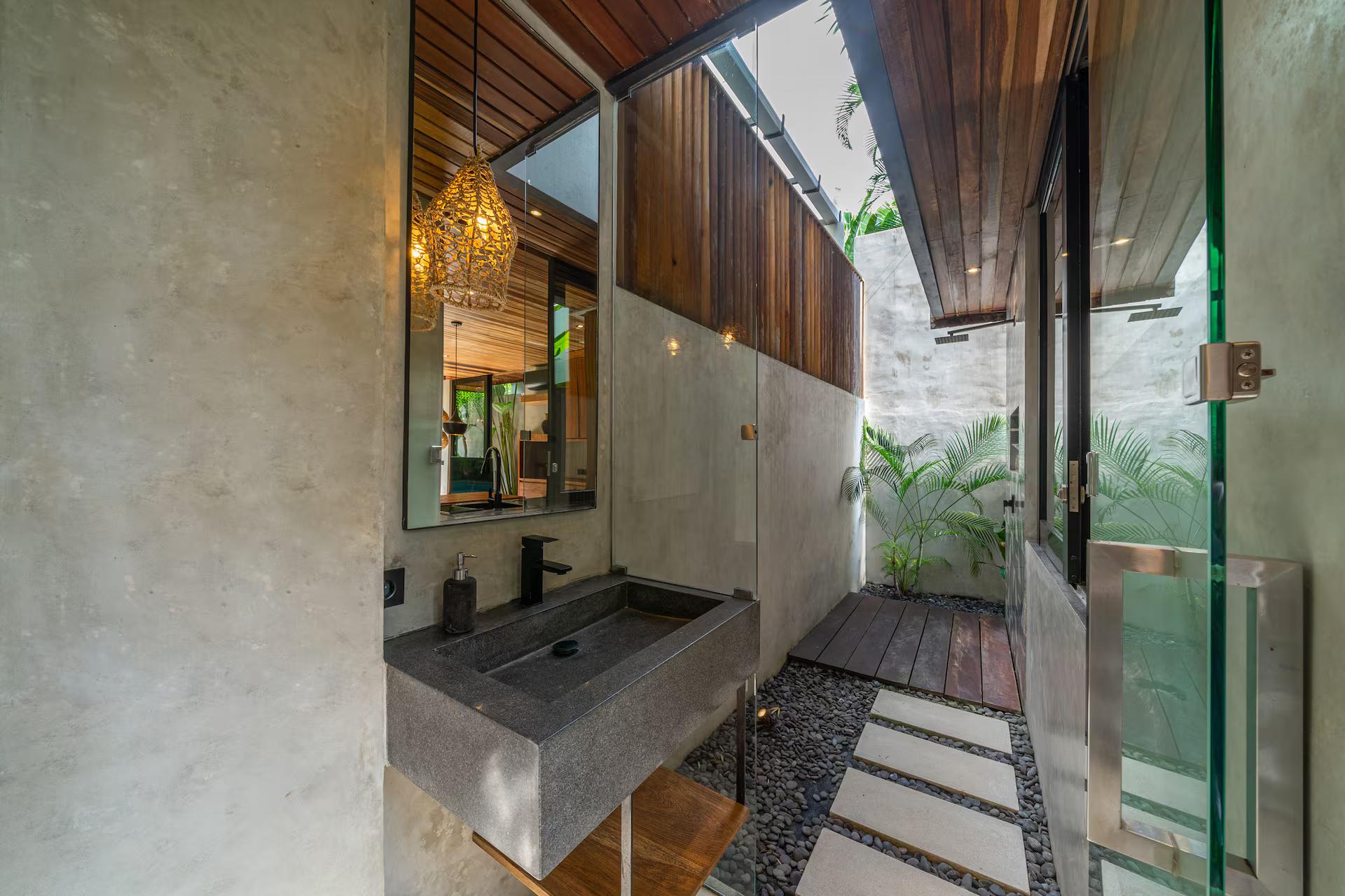 Semi-outdoor bathroom at Villa Solani with a cast-stone basin and stepping stones over pebbles