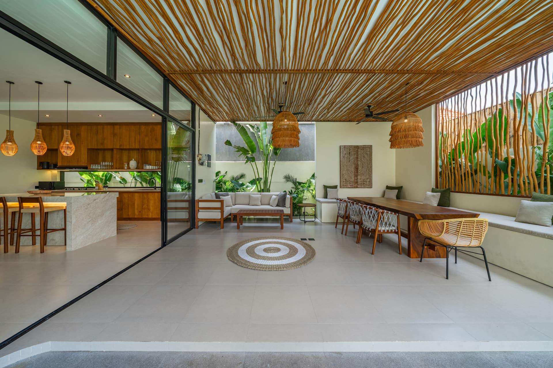 Covered terrace under a bamboo-batten ceiling with a lounge, long timber dining table and open kitchen