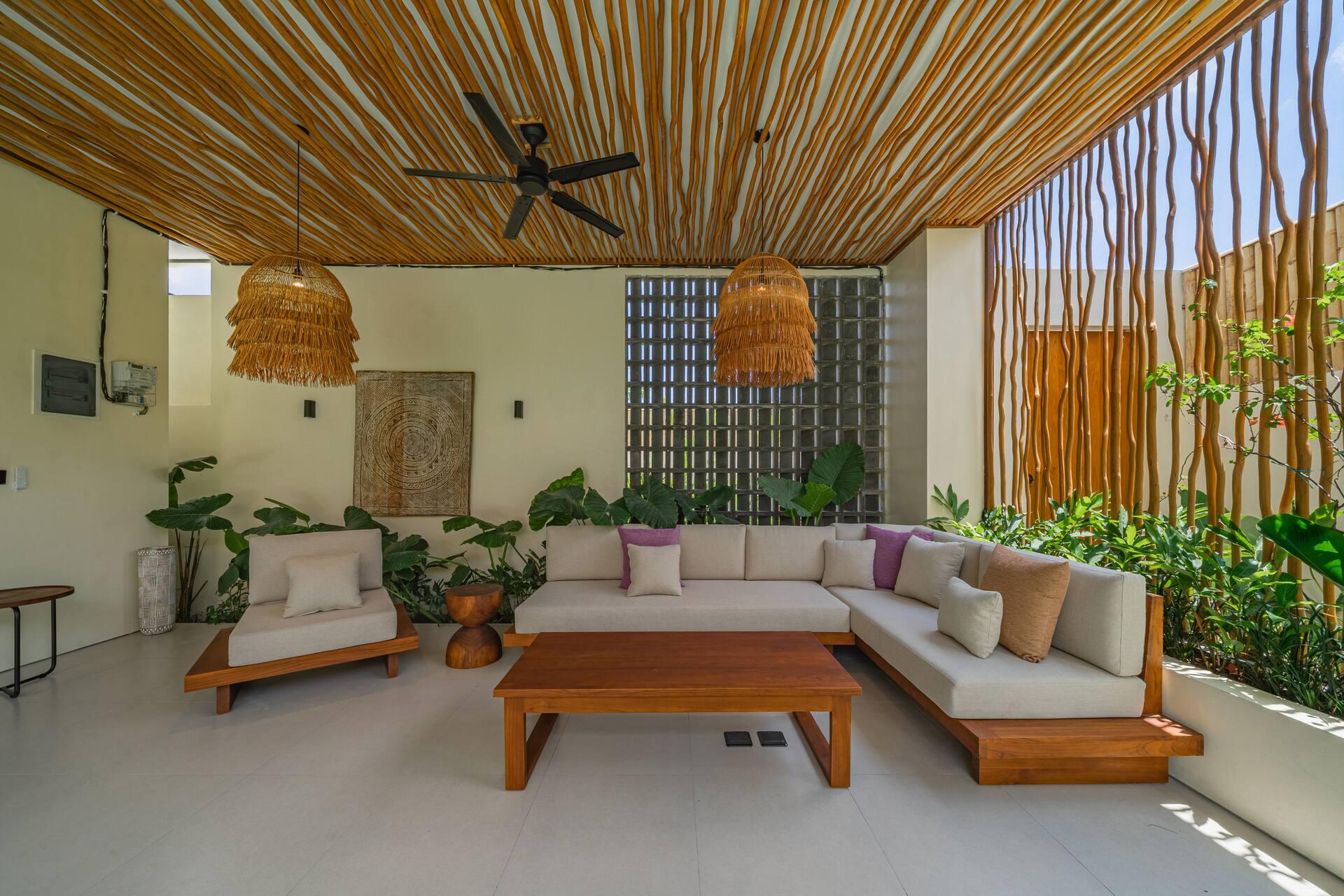 Outdoor living room with an L-shaped sofa, timber coffee table and rattan pendants under bamboo battens
