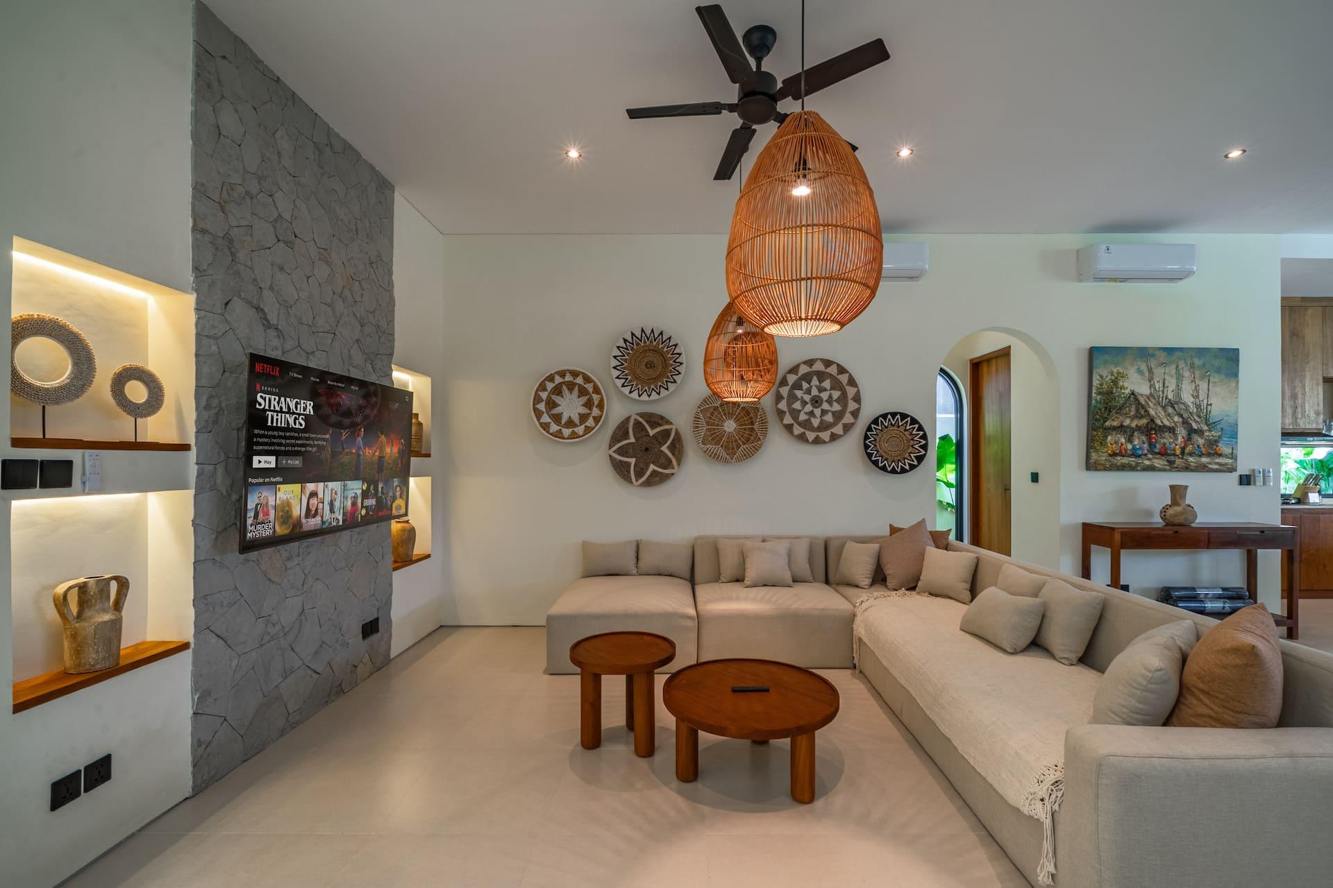 Open-plan living room with a deep L-shaped sofa, round timber tables and a stone-clad TV wall