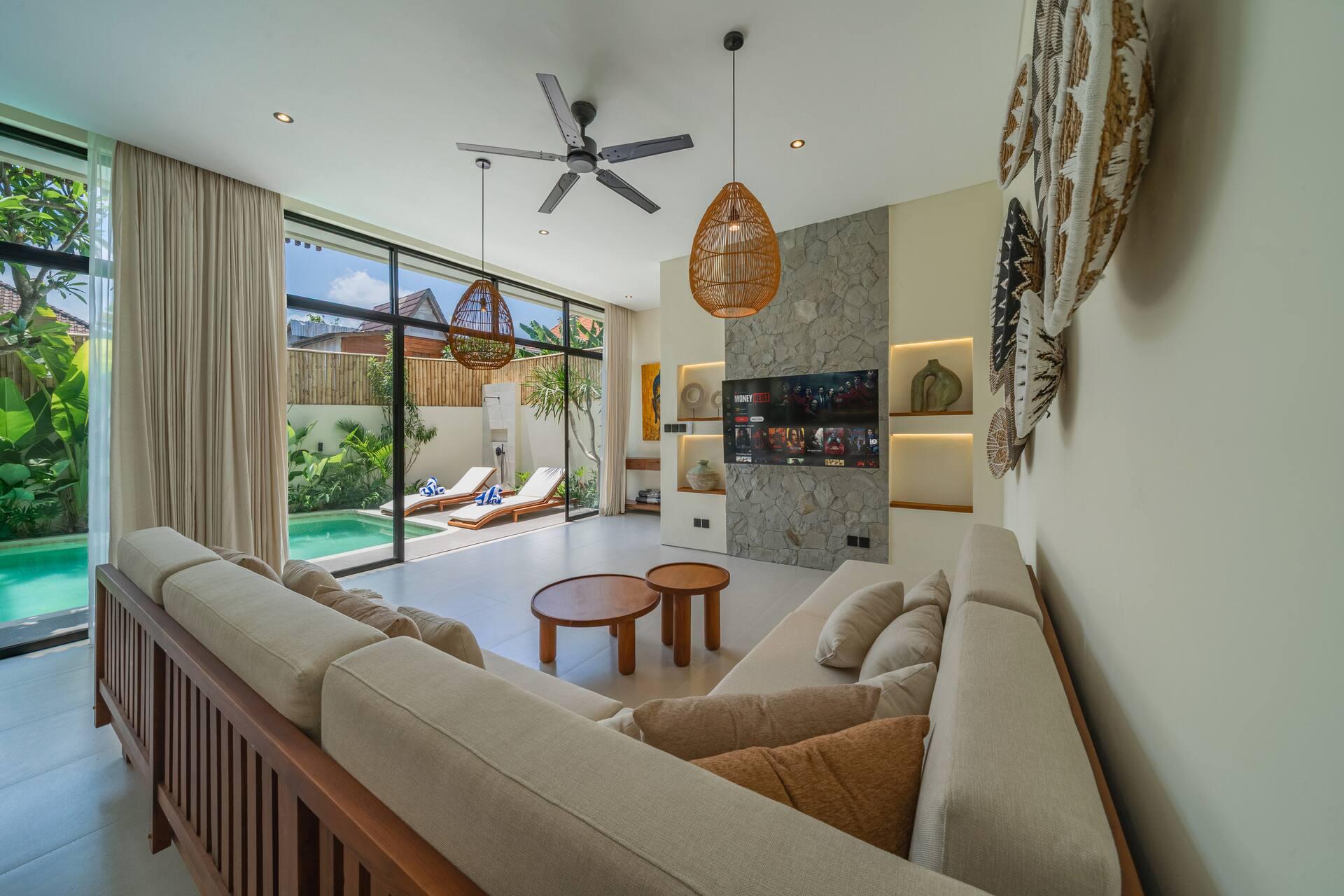 Bright living room with a long sofa, stone-clad Smart TV wall and glass doors open to the pool