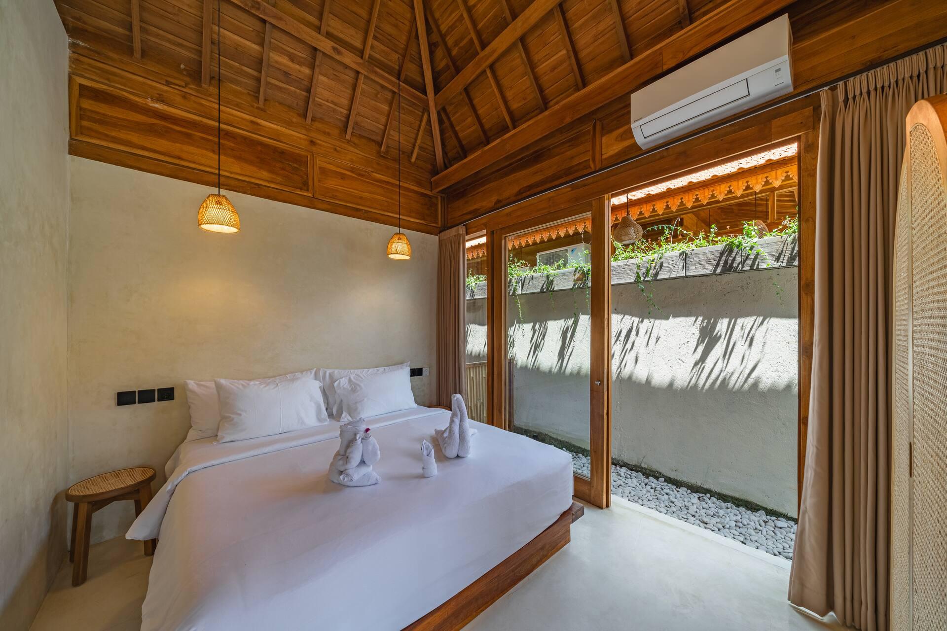 Bedroom with a pitched timber ceiling, white bedding and full-height glass onto a gravel light-well