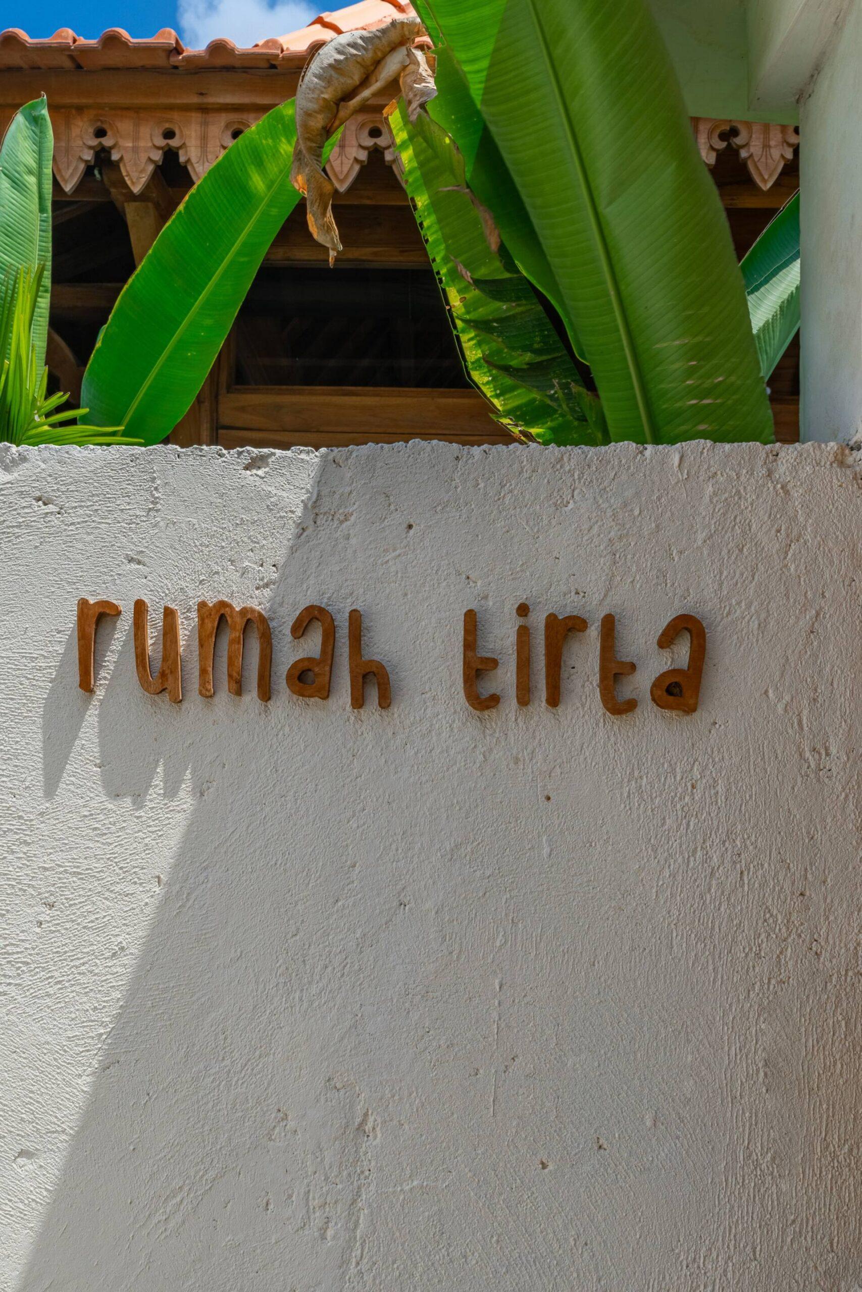 Rumah Tirta name lettered on the rendered garden wall beside banana leaves at the entrance