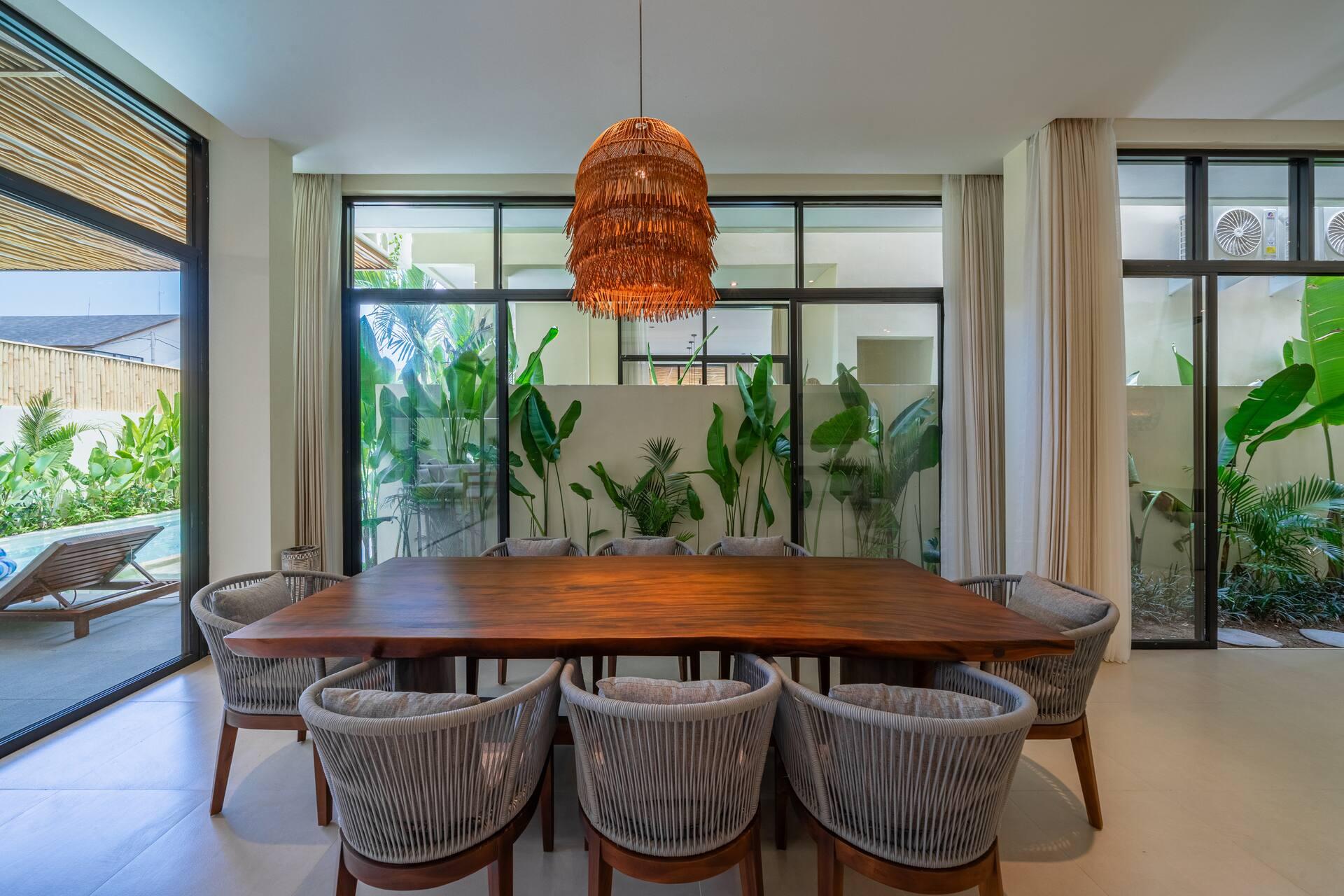 Dining table for eight with woven chairs and a rattan pendant beside full-height garden windows