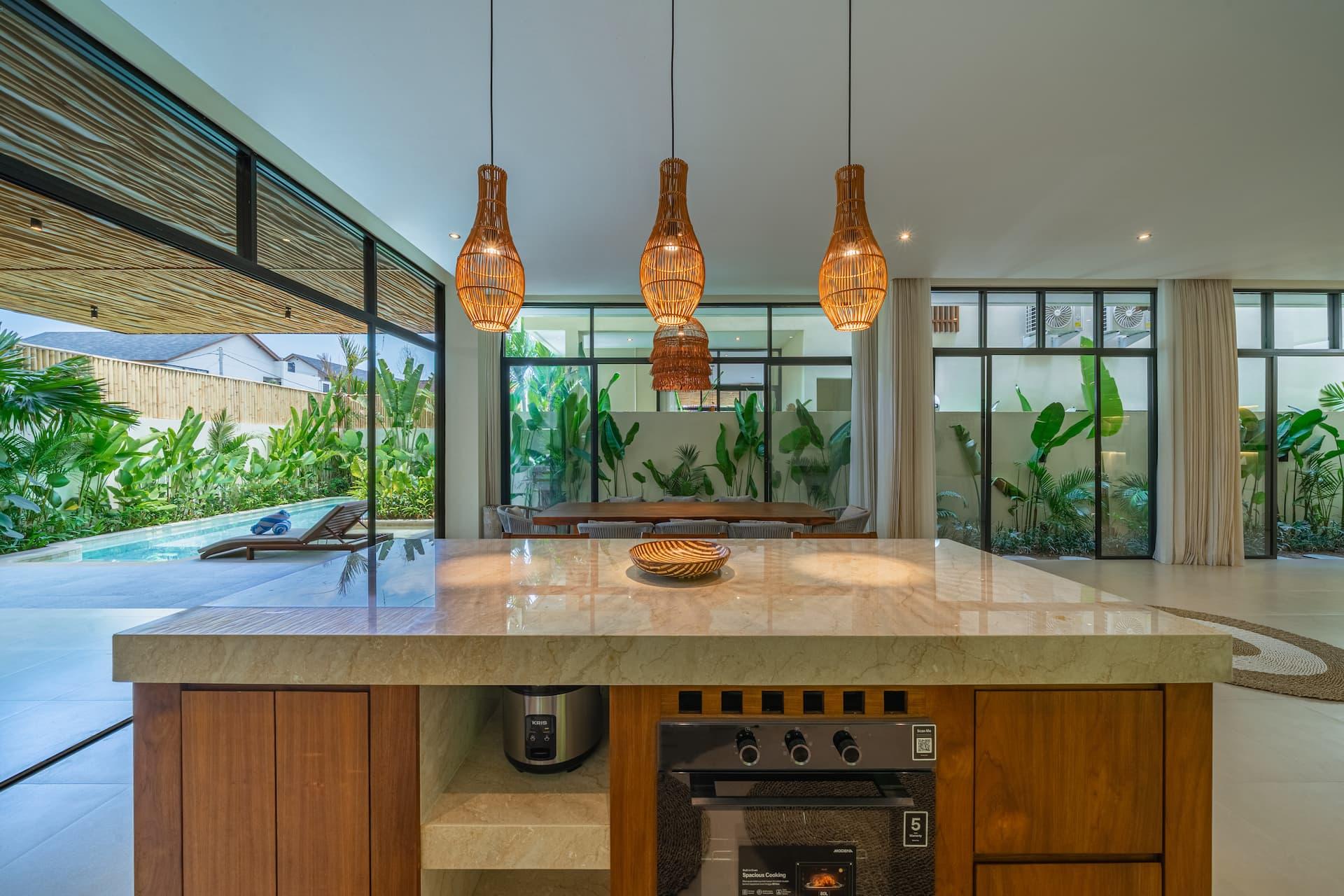 Timber kitchen with a stone-topped island, oven and a window splashback looking onto tropical planting