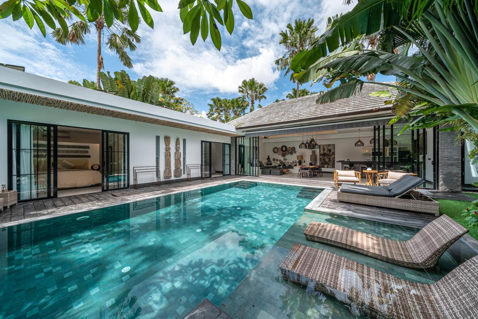The long pool at Villa Marlon with rattan loungers on the timber deck and palms overhead