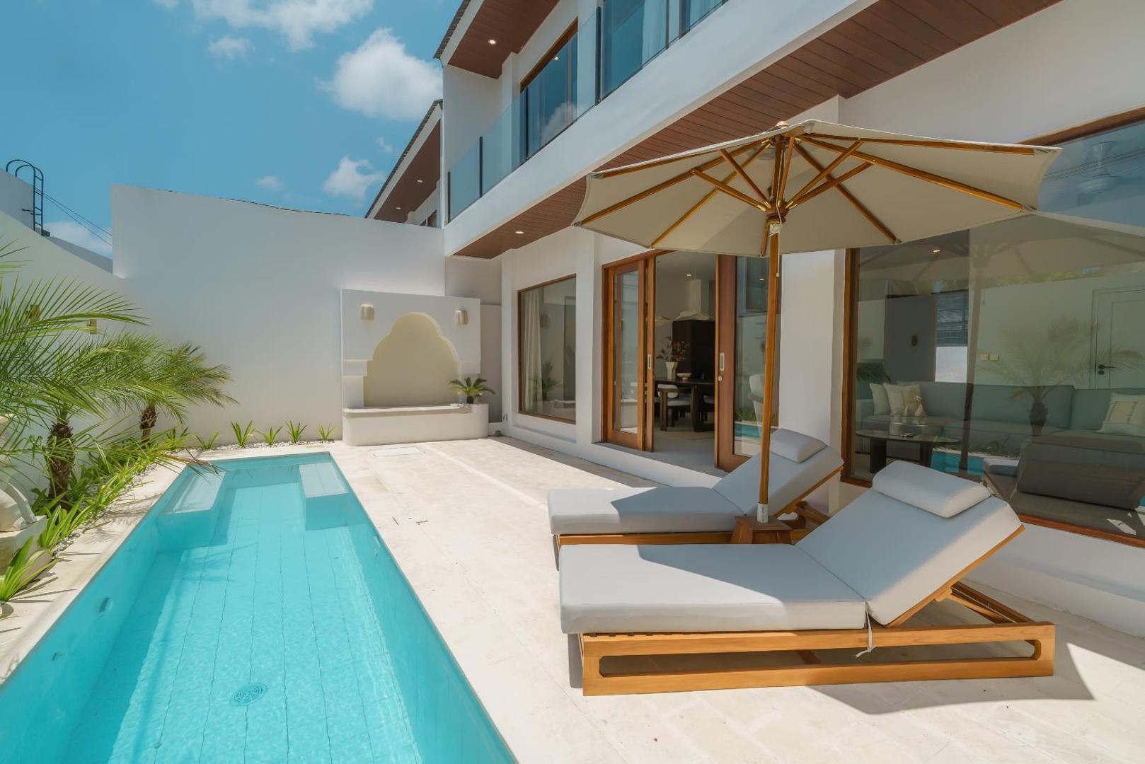 The lap pool at Villa Umaju, timber loungers and a canvas parasol on travertine paving