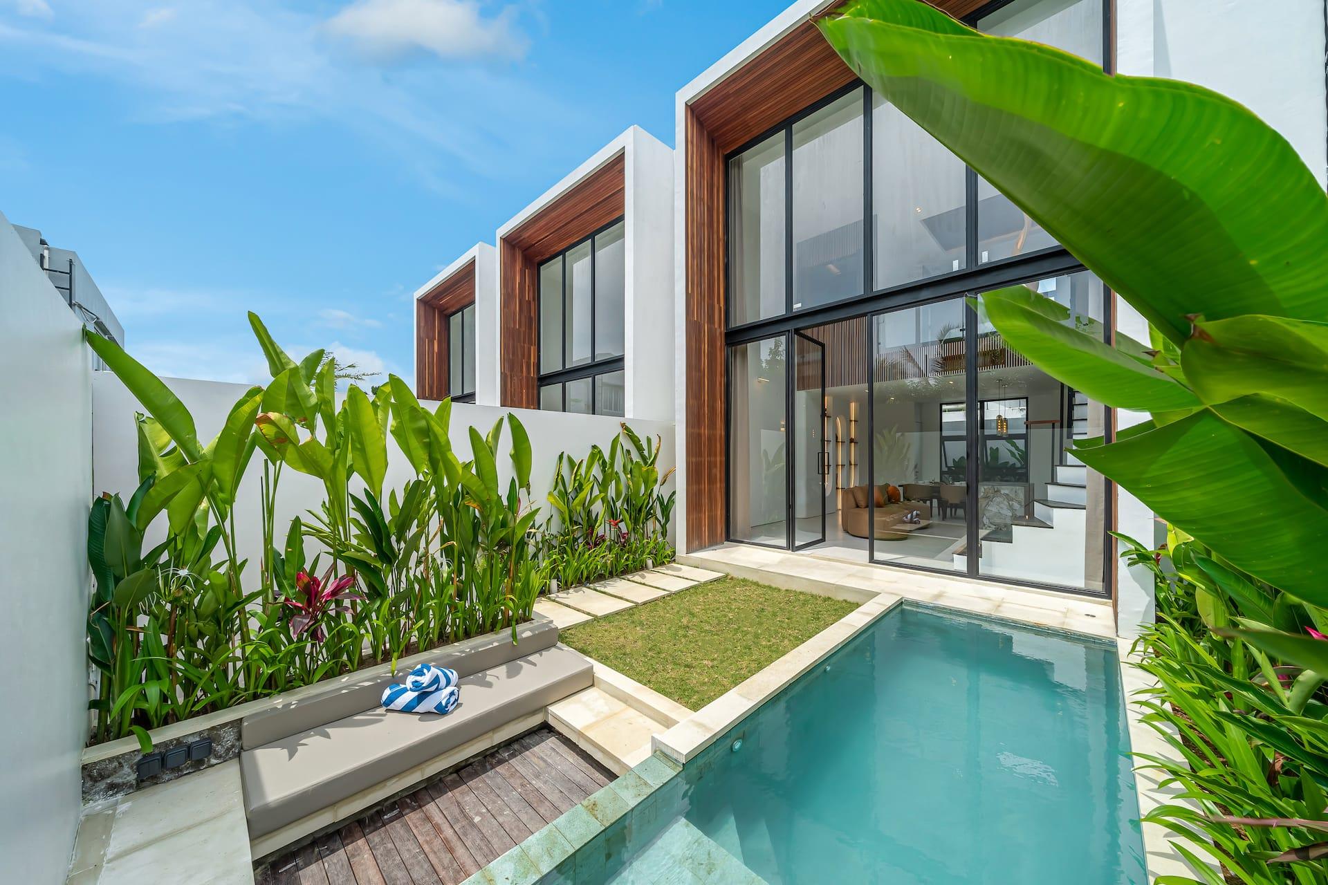 Fire Villa Berawa seen across its private pool, timber-clad upper storey and heliconia-planted lawn