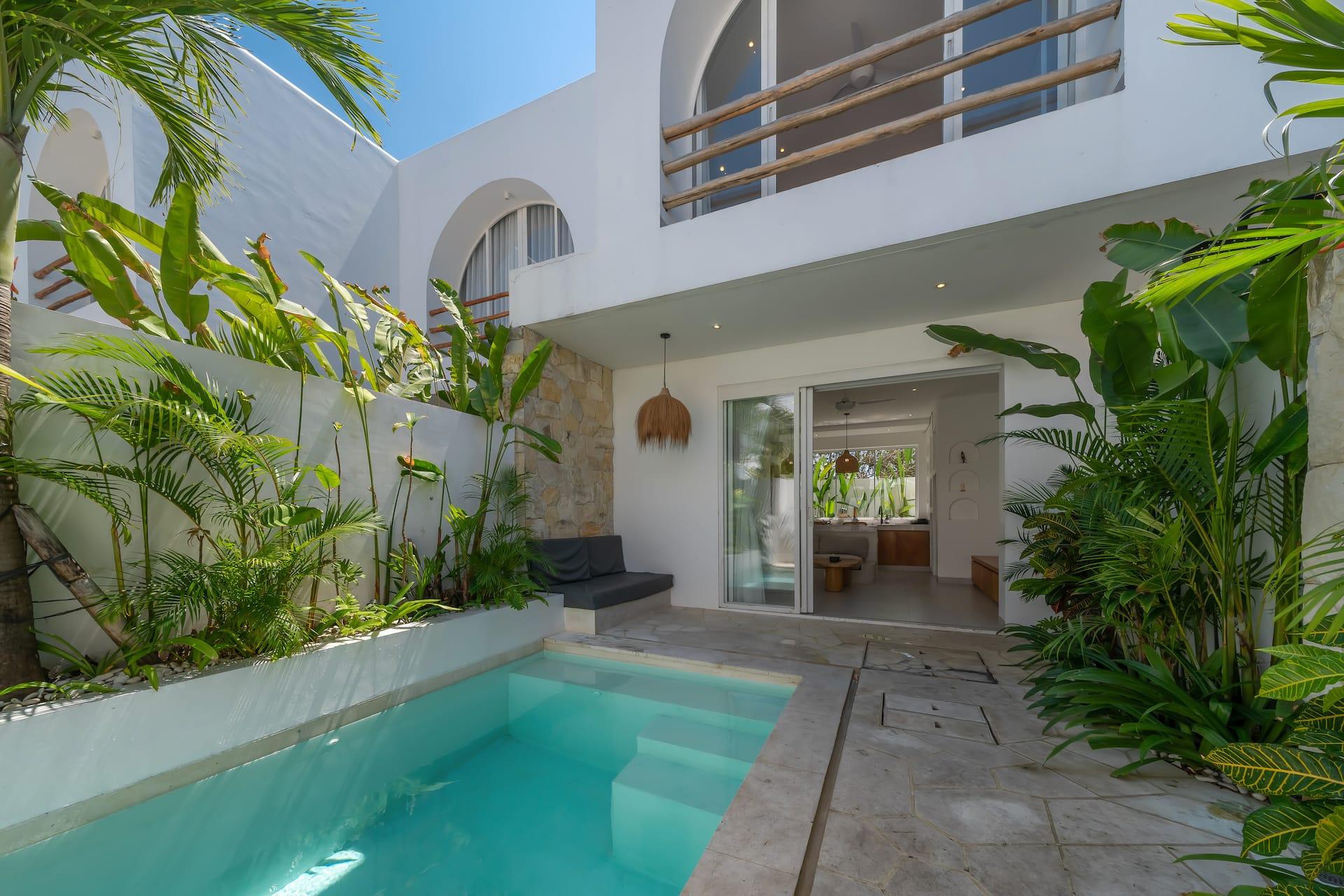 The pool at Las Casas 5 set in travertine paving, with the whitewashed villa and its arched openings behind