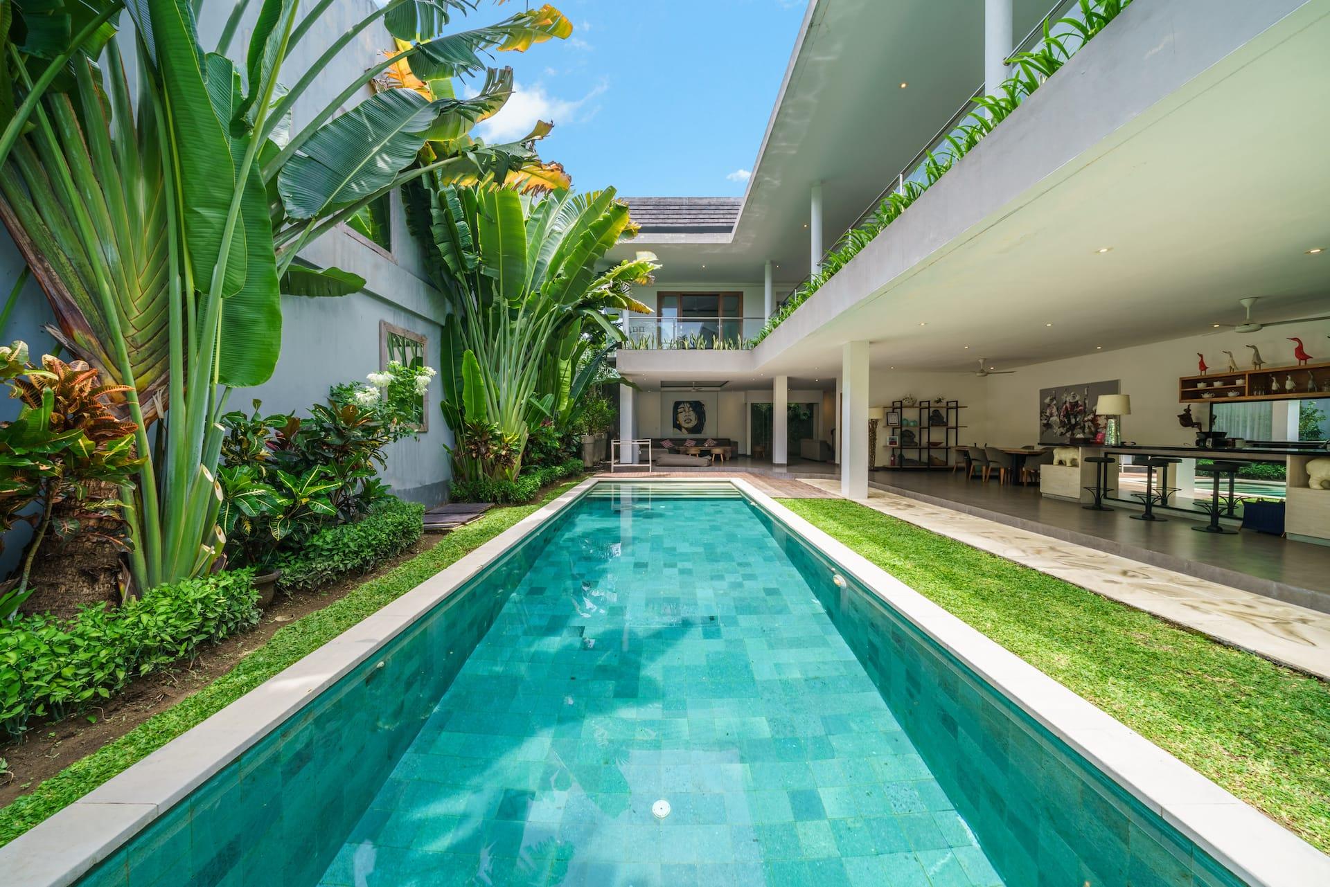 Villa Paloma's green-tiled lap pool with lawn on one side and the open living floor beyond
