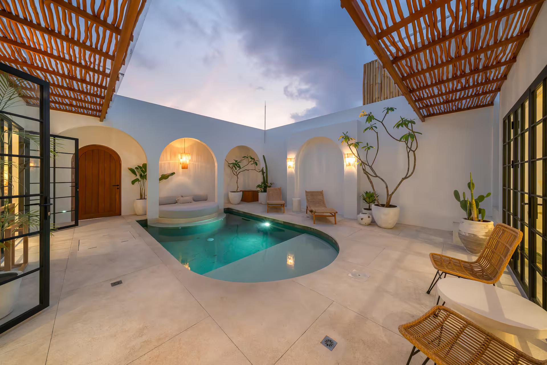 The curved courtyard pool at Villa Valeria at dusk, lit beneath a bamboo pergola and white plaster arches