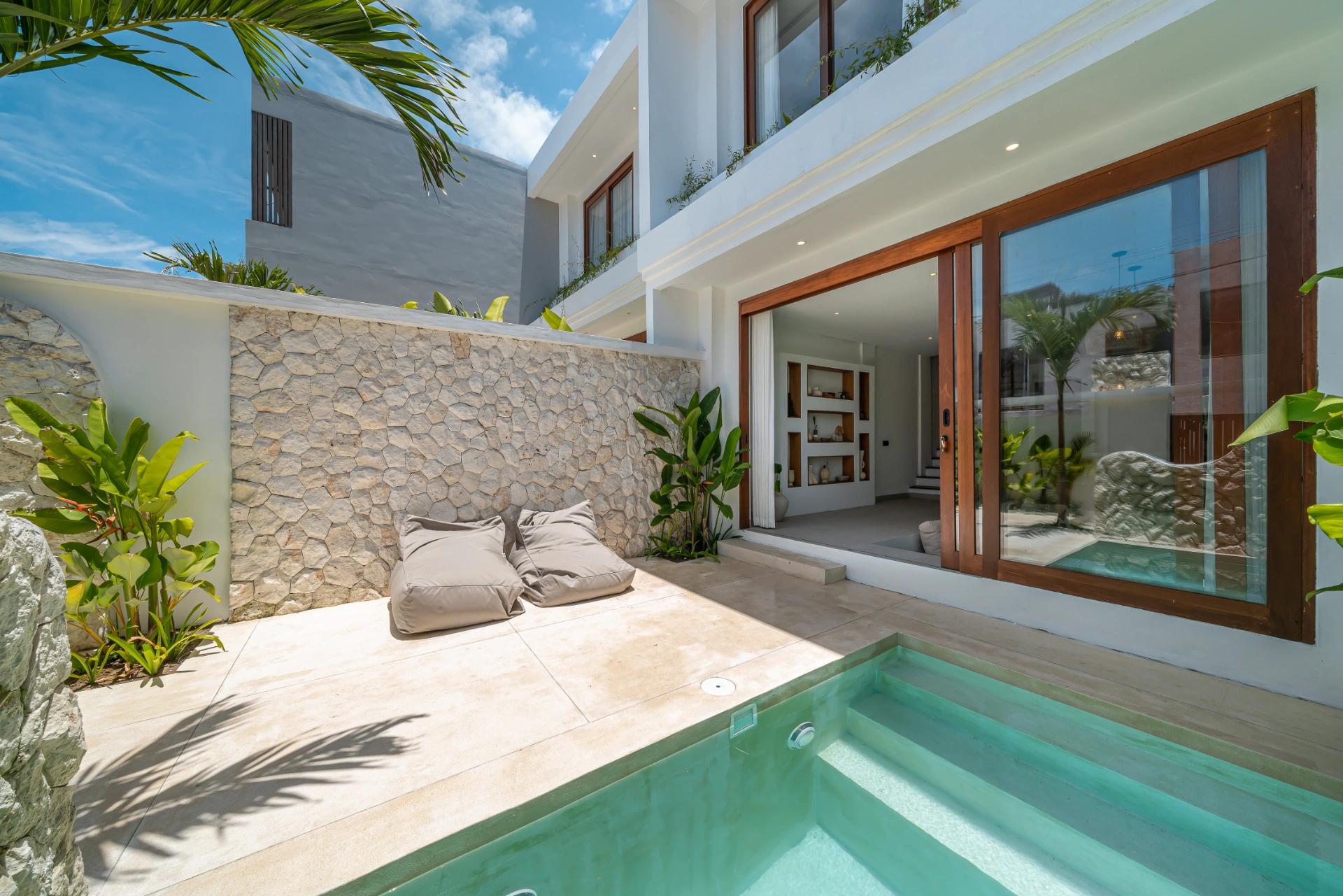 The pool at Villa Kembali 10, travertine deck and beanbags below a rough coral-stone wall