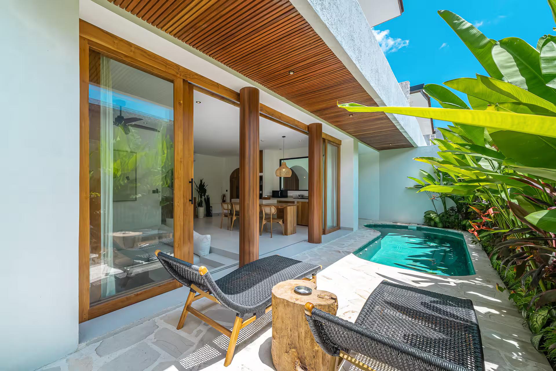 The slim pool at Villa Rindu Kamu, mesh loungers on stone paving beneath timber posts