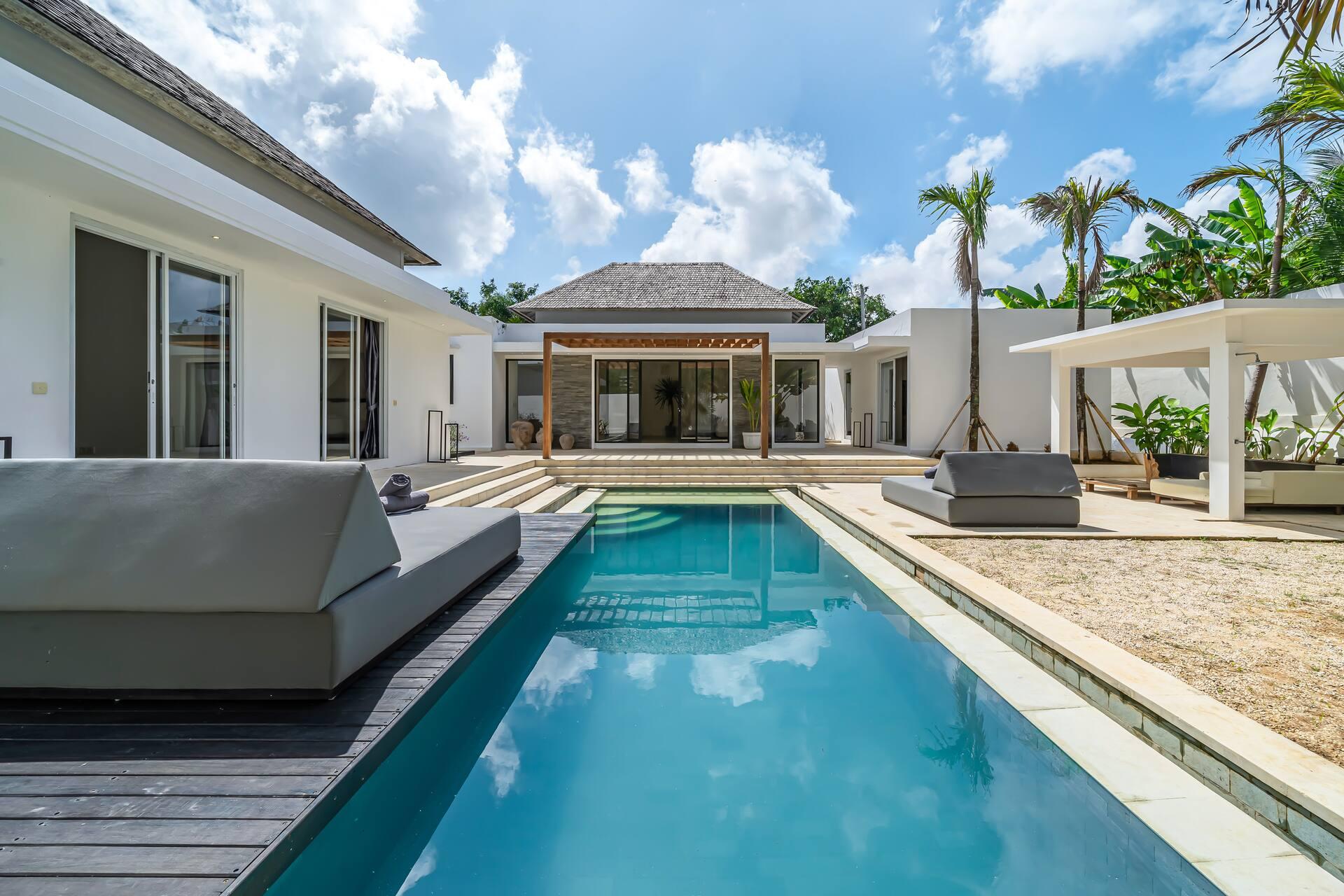 Villa Zenaya's long pool leading to a hip-roofed pavilion, with grey daybeds on a dark timber deck