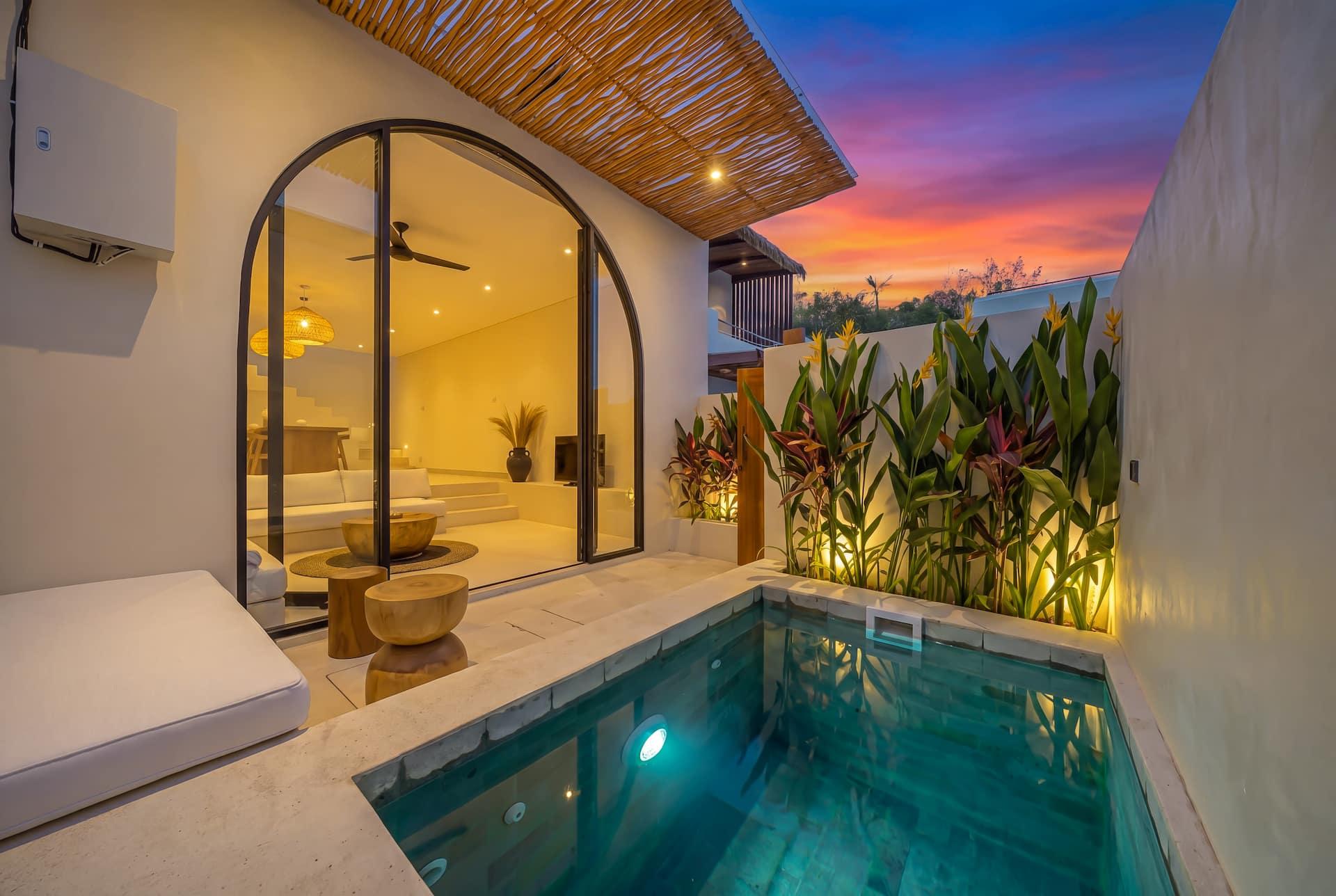 Villa Adiwarna at dusk, a green-tiled plunge pool below arched glass doors and lit tropical planting