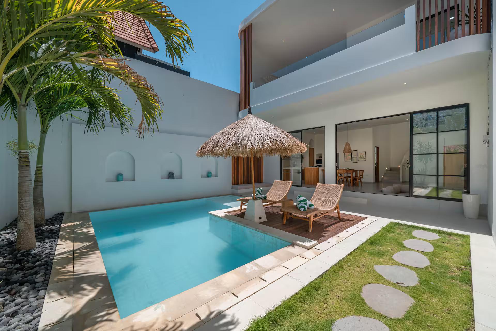The pool at Villa Yuri with its thatched parasol, lawn and stepping stones alongside