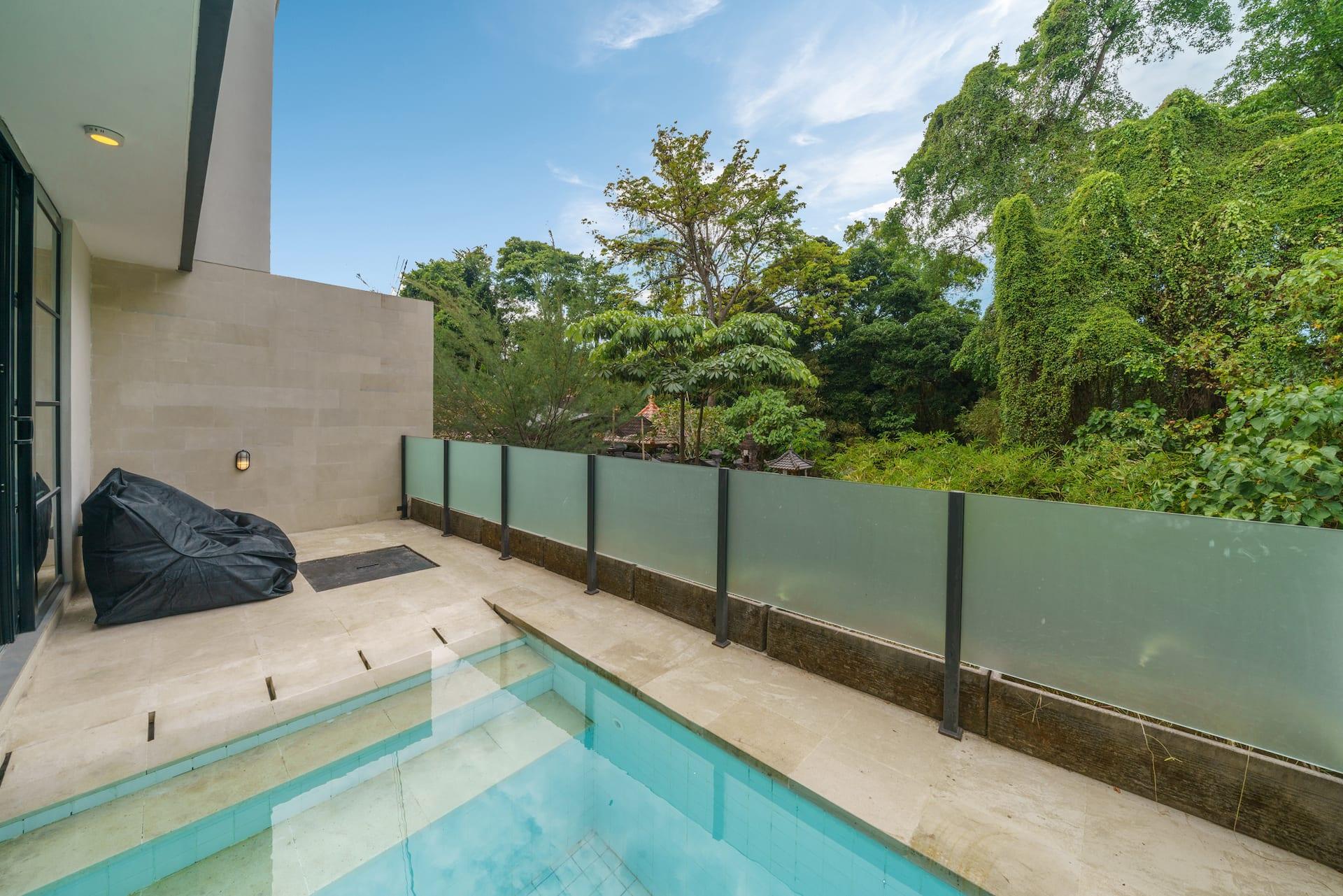 Loft Valentin's private plunge pool behind a frosted glass balustrade, looking out over tall jungle trees