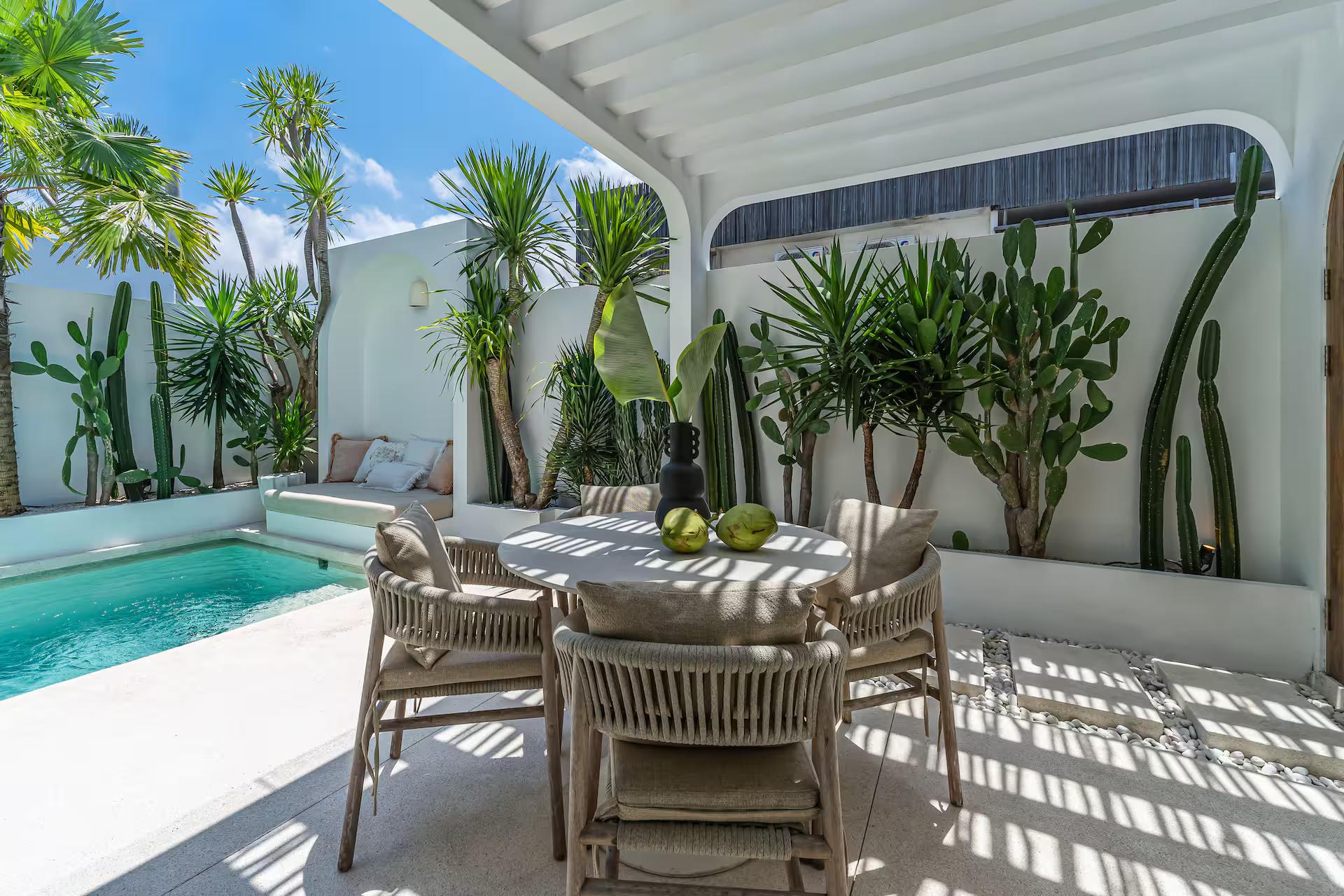 Outdoor dining table and rattan chairs in striped pergola shade beside the pool