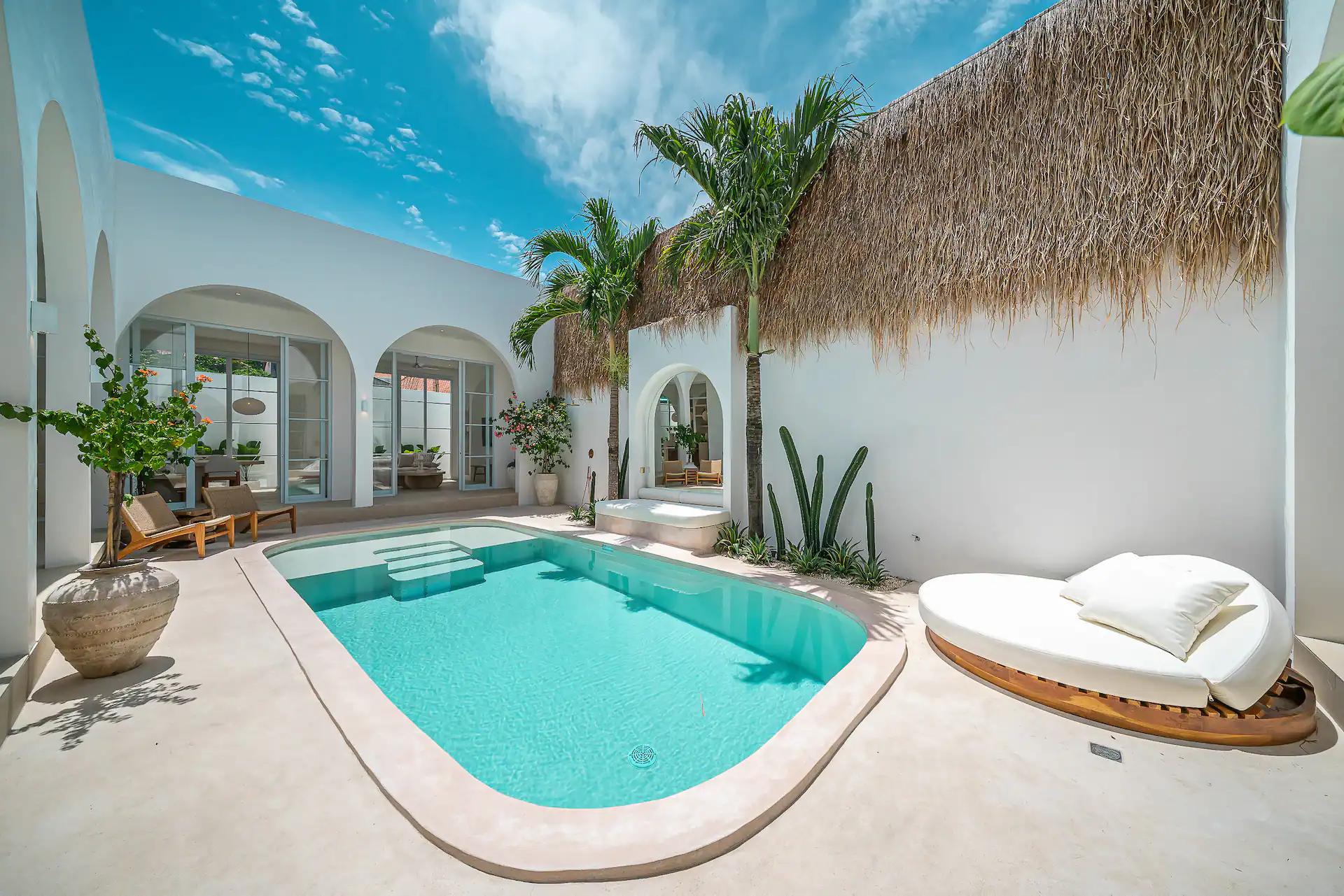 Sunken plaster daybed at the pool edge beneath a wall of alang-alang thatch