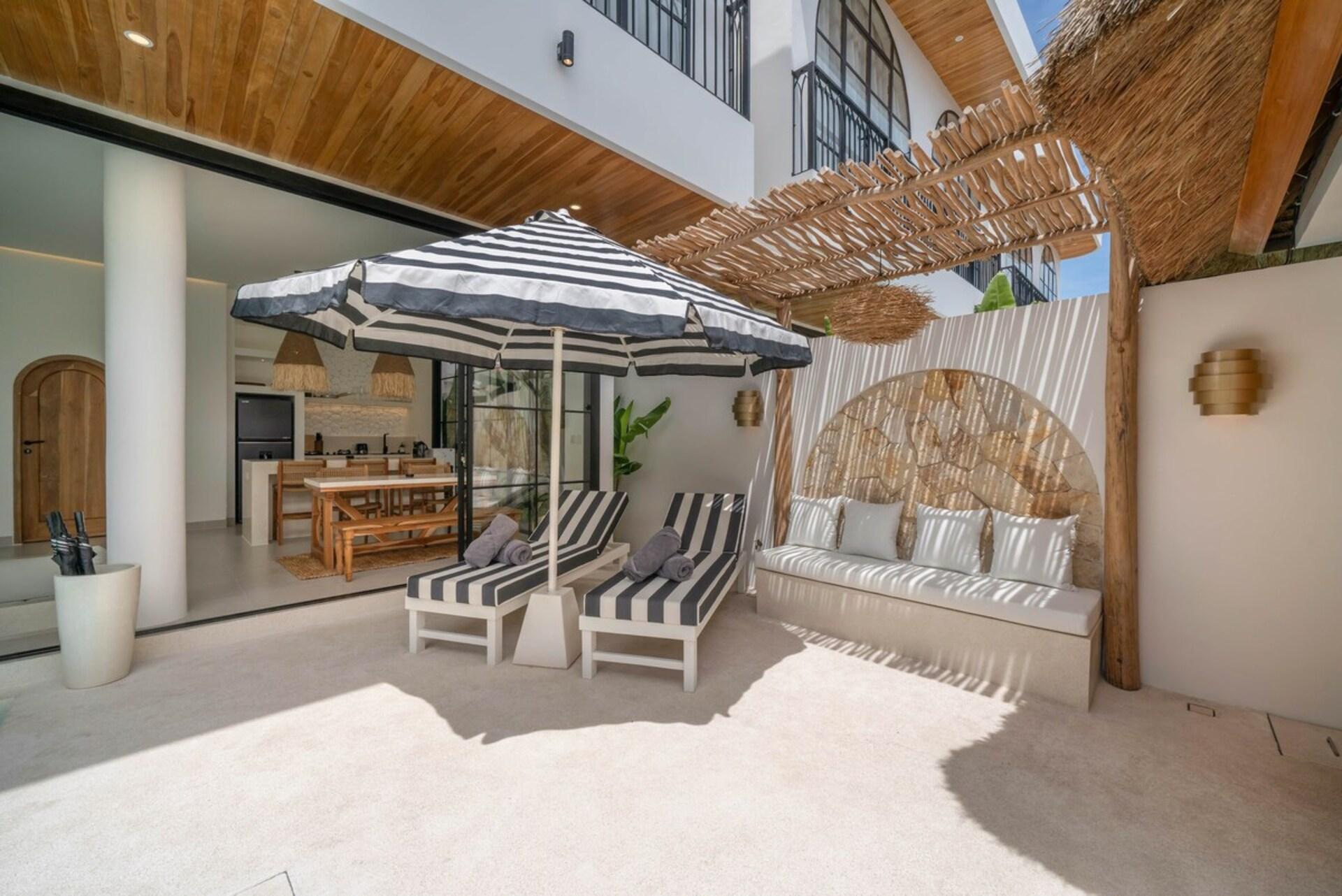 Pool deck lanai with striped sun loungers, a parasol and a rattan-backed daybed