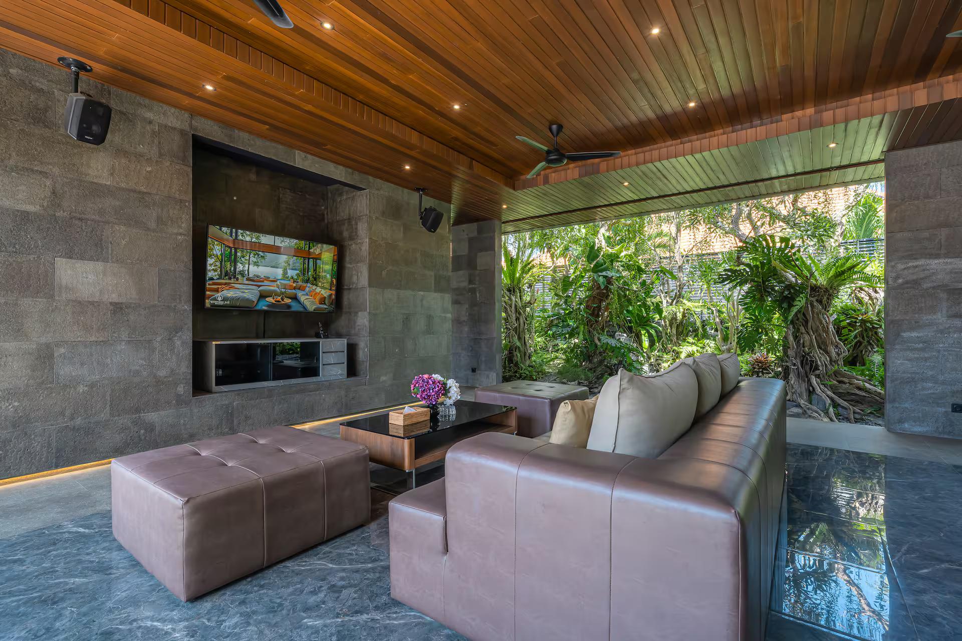 Covered outdoor lounge with deep sofas and a wall-mounted screen facing the garden