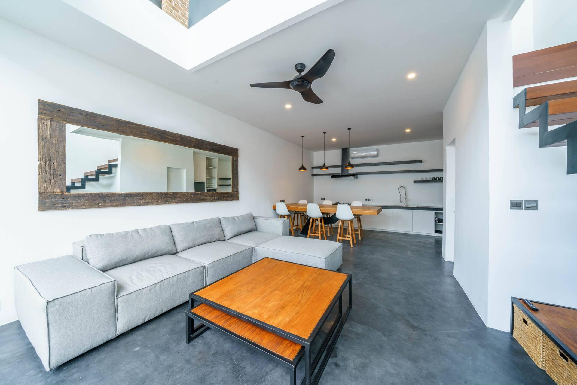 Grey sectional and steel-framed coffee table on polished concrete, dining beyond