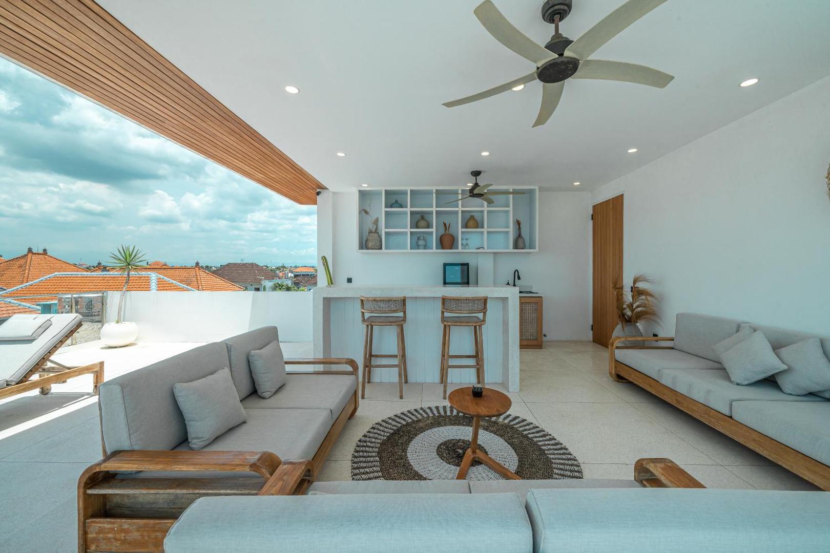 Rooftop lounge with a timber bar counter, built-in daybeds and the rooftops of Canggu beyond