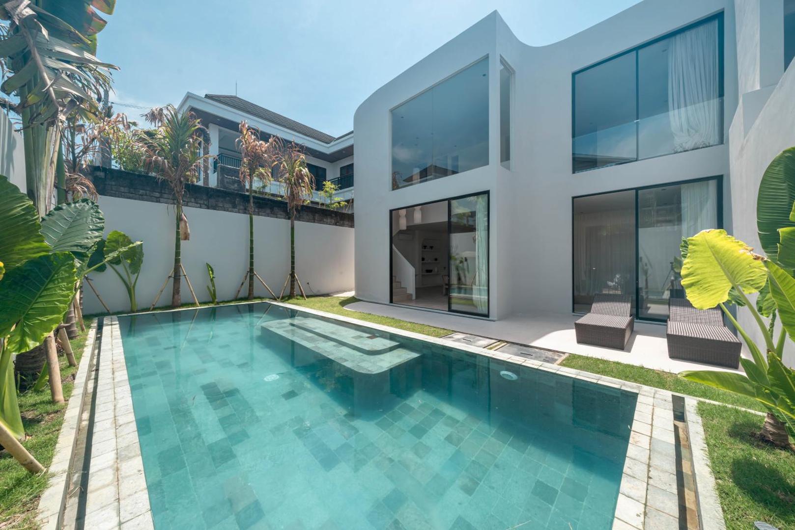 Sun loungers on the paved terrace beside the long lap pool, lawn running the length of the garden