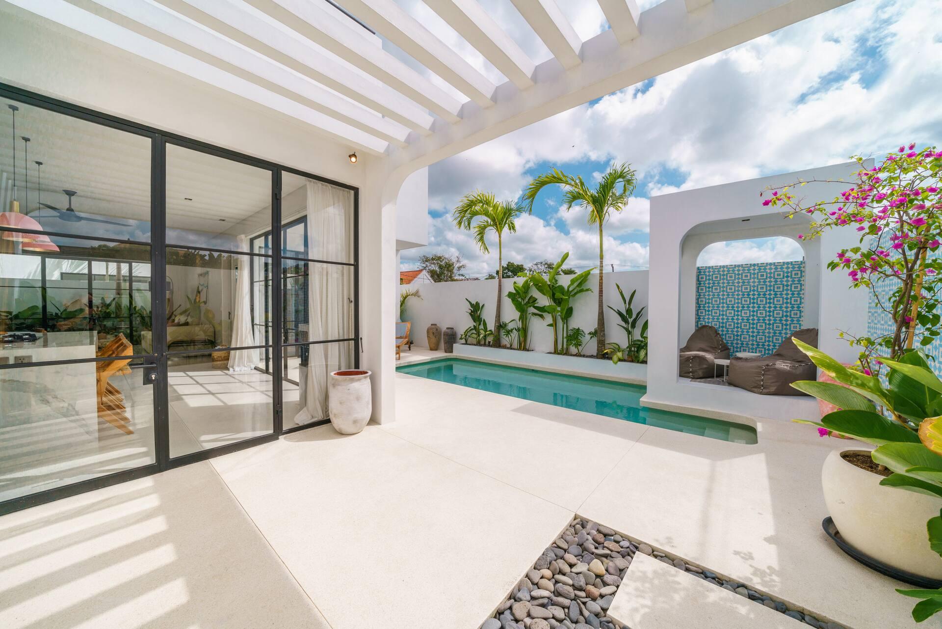 Covered terrace on white pergola beams beside the pool, arched mosaic daybed niche behind