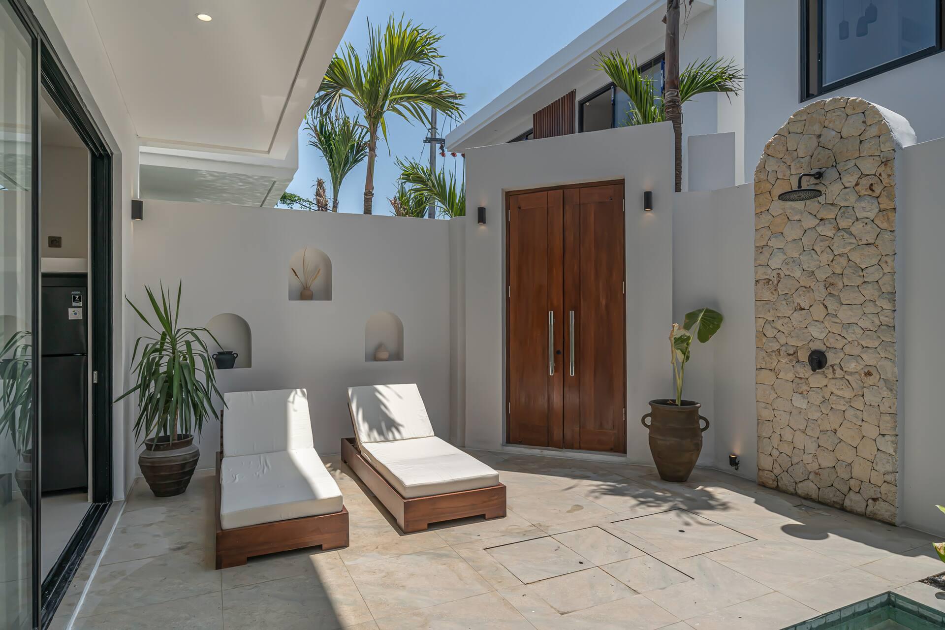 Terrace loungers beside the timber entrance doors, a rough stone panel carrying the outdoor shower