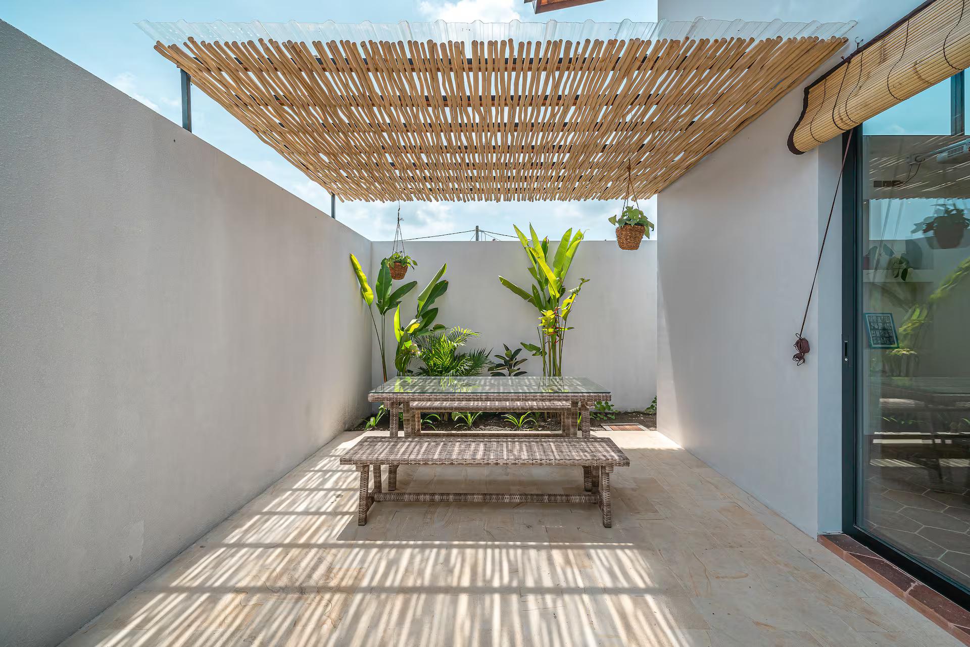 Bamboo pergola throwing striped shade over a timber bench table in the side courtyard