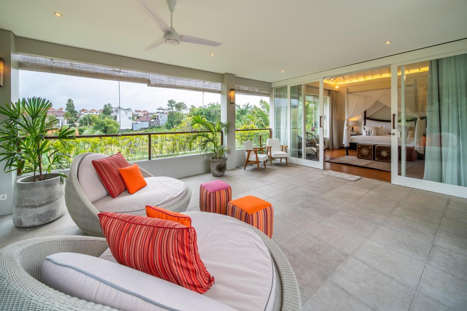Round rattan daybed with red and orange cushions on the upper terrace, beside a bedroom door