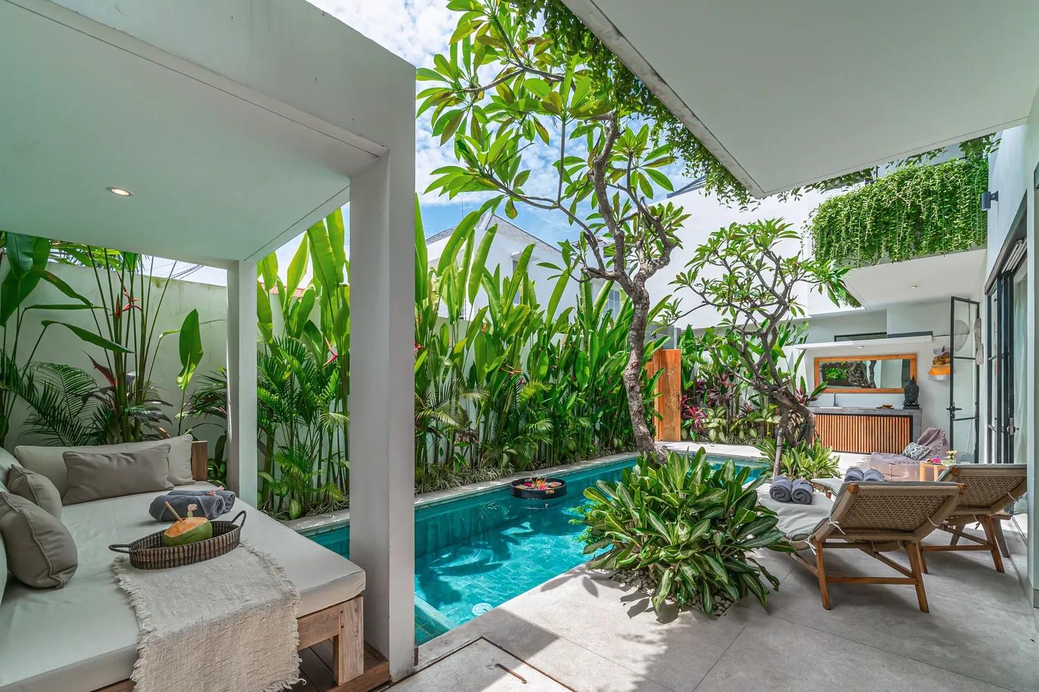 A cushioned daybed in the shaded bale at the far end of the pool, coconut on a rattan tray
