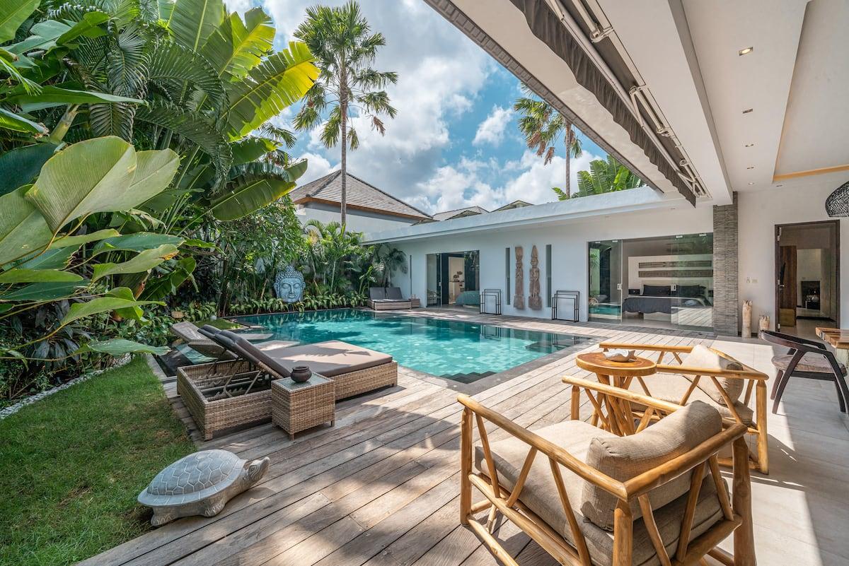 Timber armchairs and a sun lounger on the strip of lawn beside the pool deck